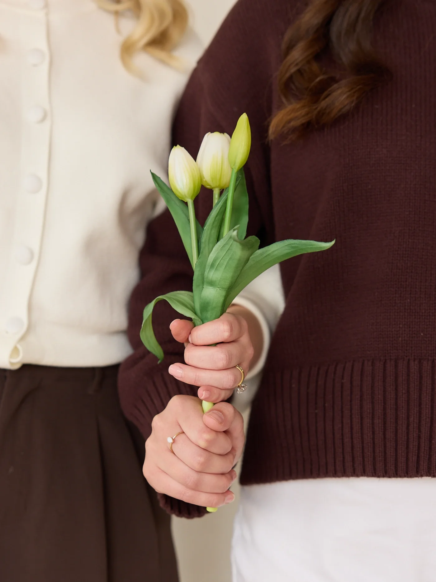Two women holding a small bouquet of three white tulips with green leaves.