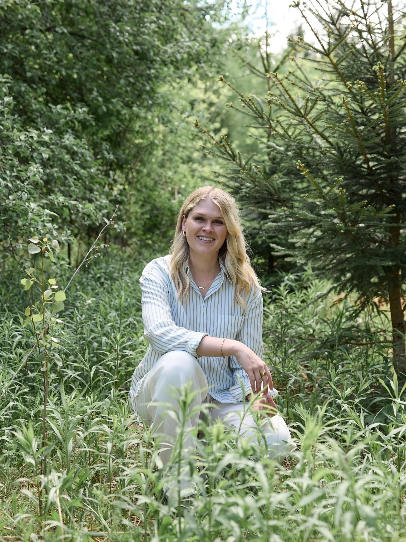 Katelyn of Ripple Effect Psychotherapy in Hamilton, Ontario sitting among green plants in a lush outdoor setting, smiling at the camera.
