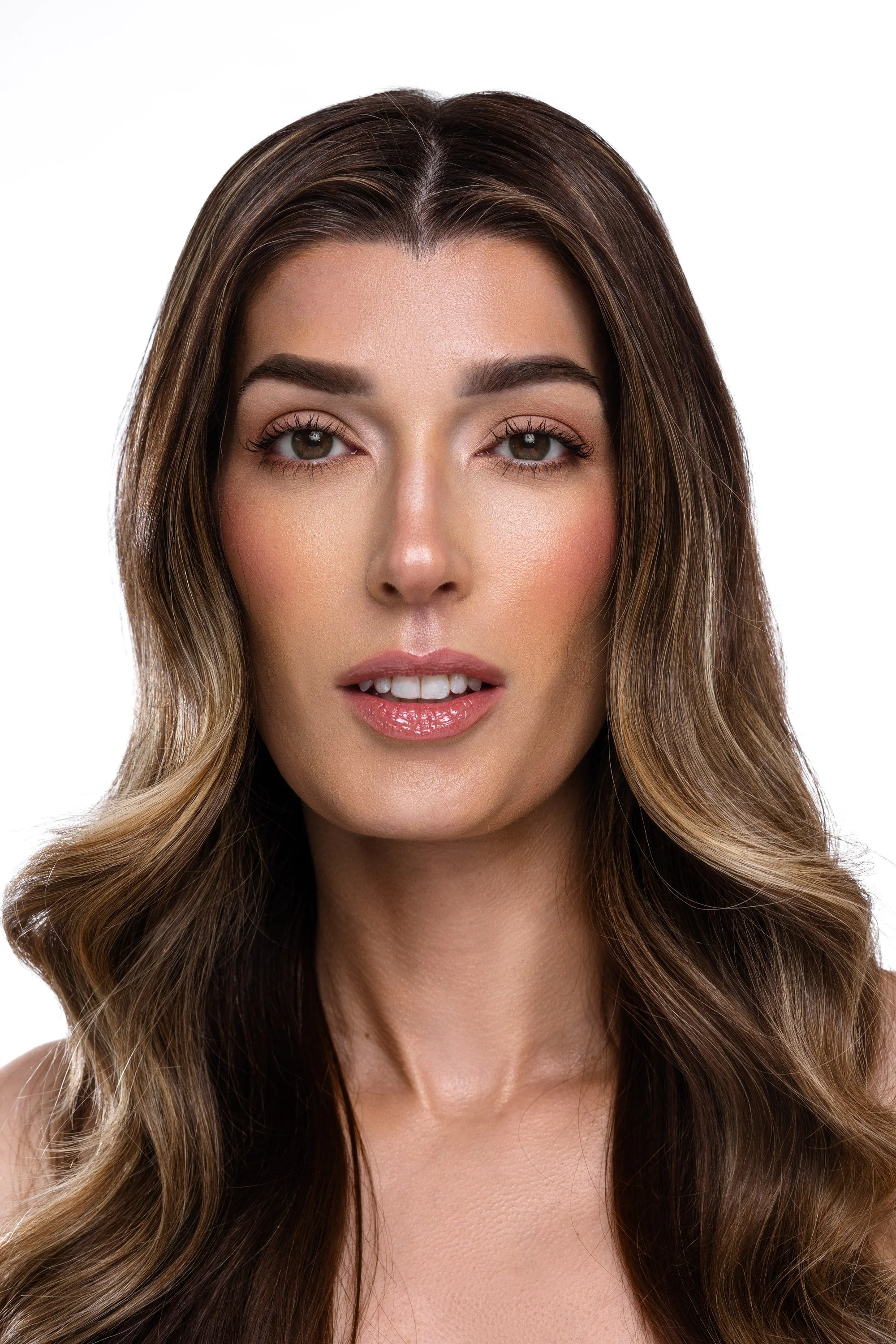 Close-up of a woman with long, wavy brown hair and light makeup, looking directly at the camera.