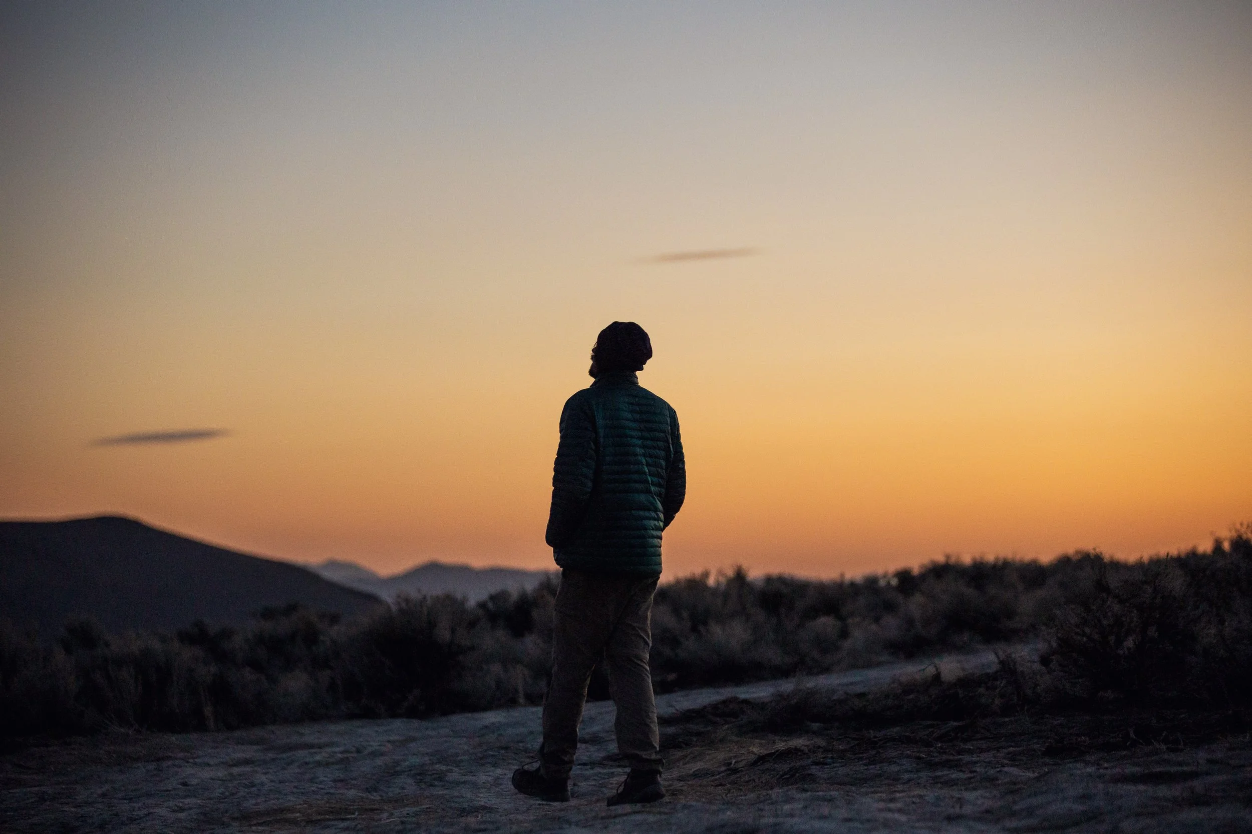 A person standing on a trail in a desert landscape during sunset.