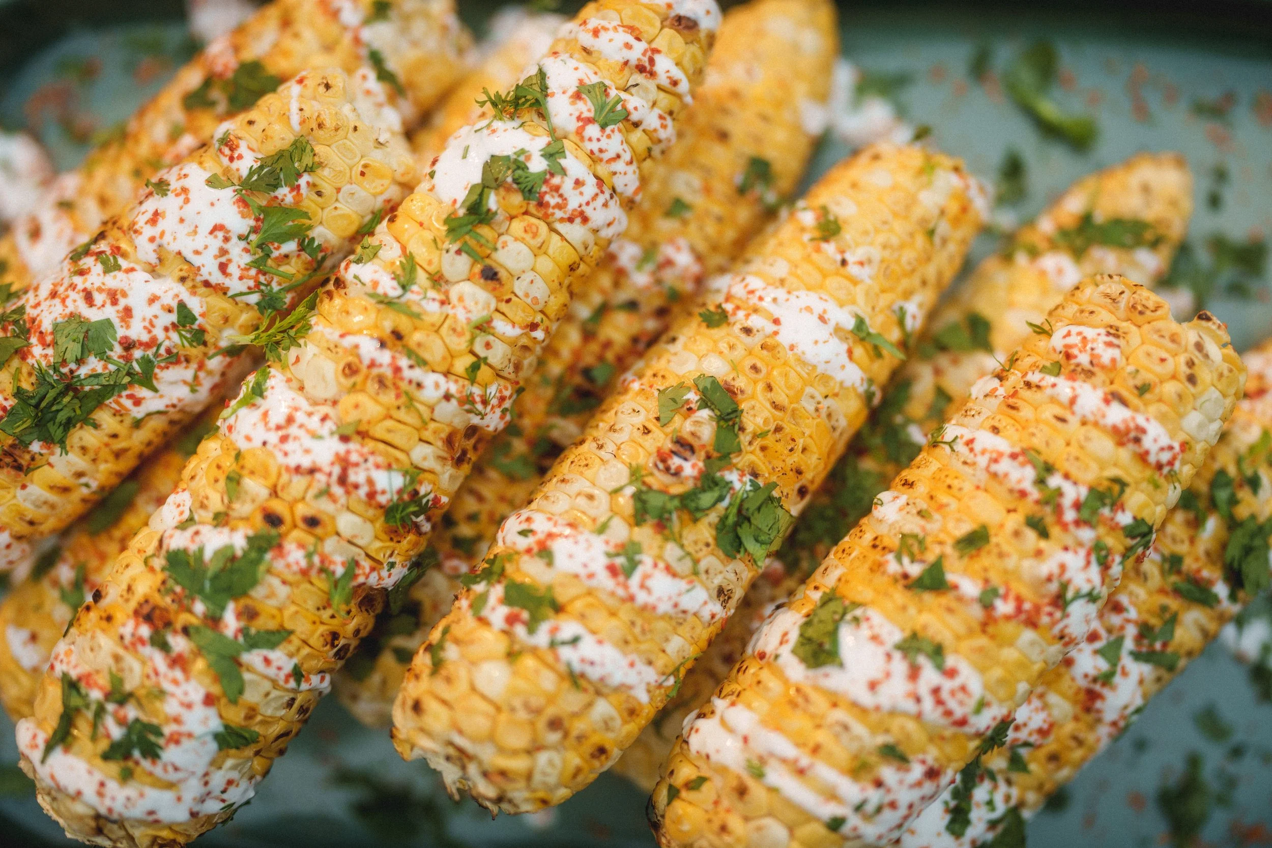 Close-up of grilled corn on the cob topped with mayonnaise, chili powder, and chopped cilantro.