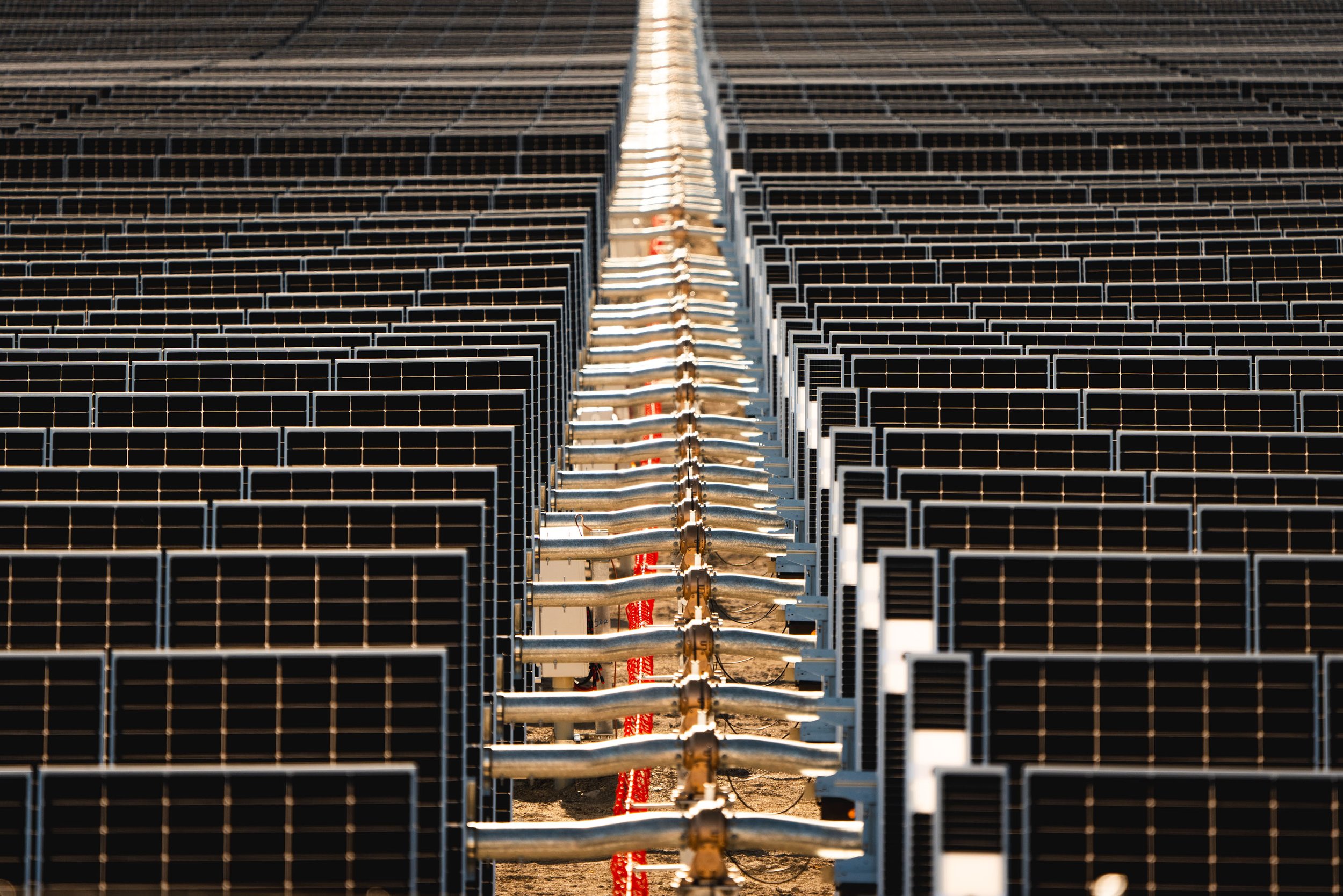 A large solar panel installation with rows of black solar panels and a metal conduit running down the center.