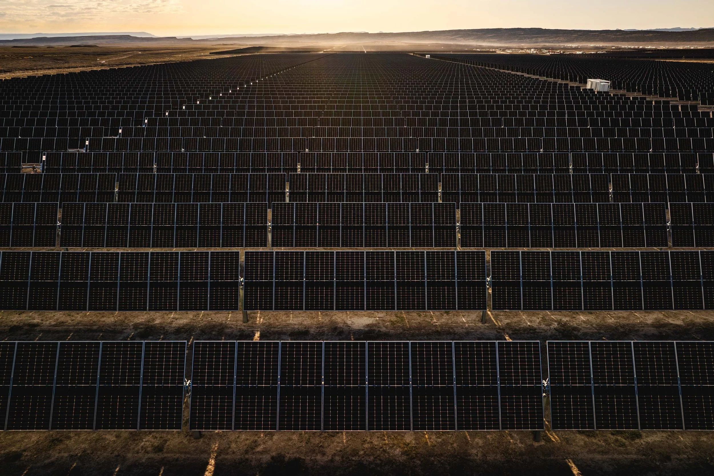 A large solar farm with multiple rows of solar panels in a desert landscape at sunset.