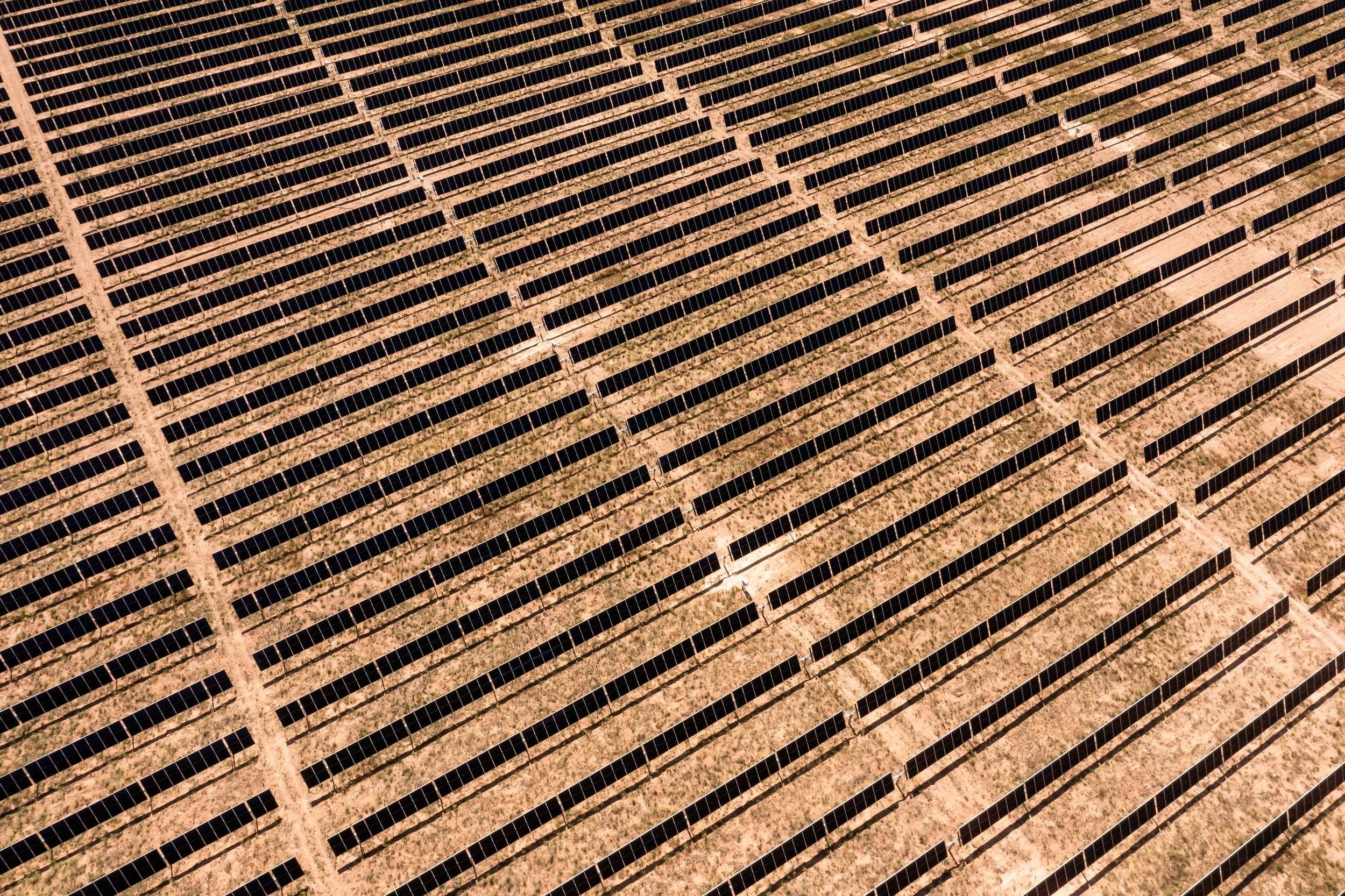 Aerial view of a solar farm with rows of solar panels in a desert landscape.
