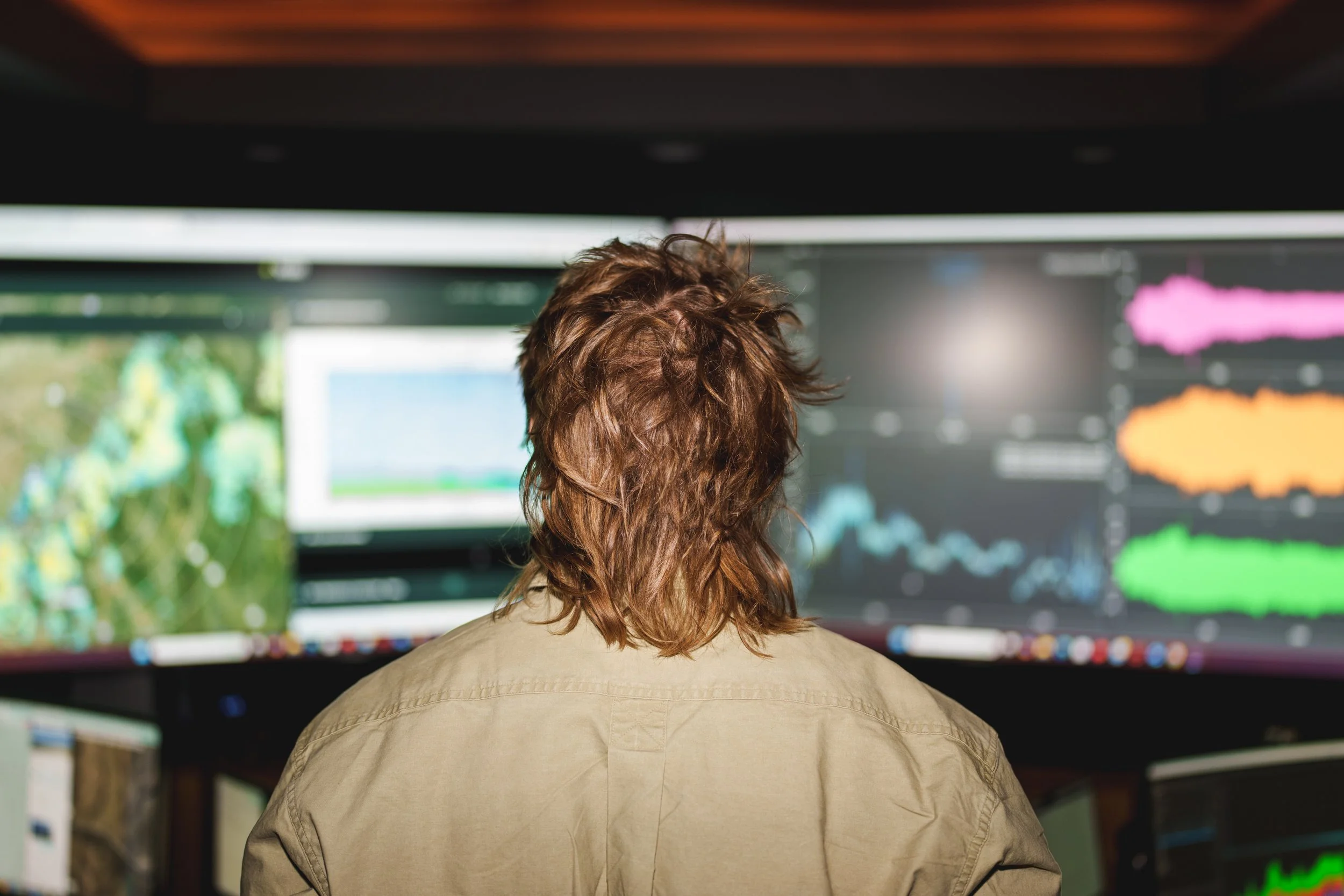 Person with brown hair working at multiple computer monitors displaying graphs and charts.