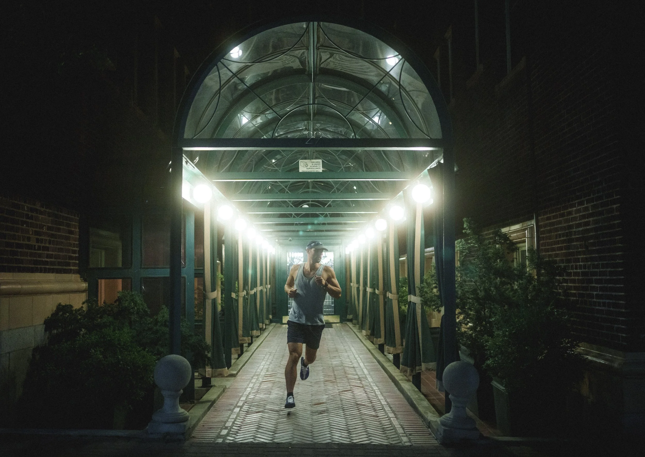 A man running at night under a illuminated archway, wearing athletic clothing.