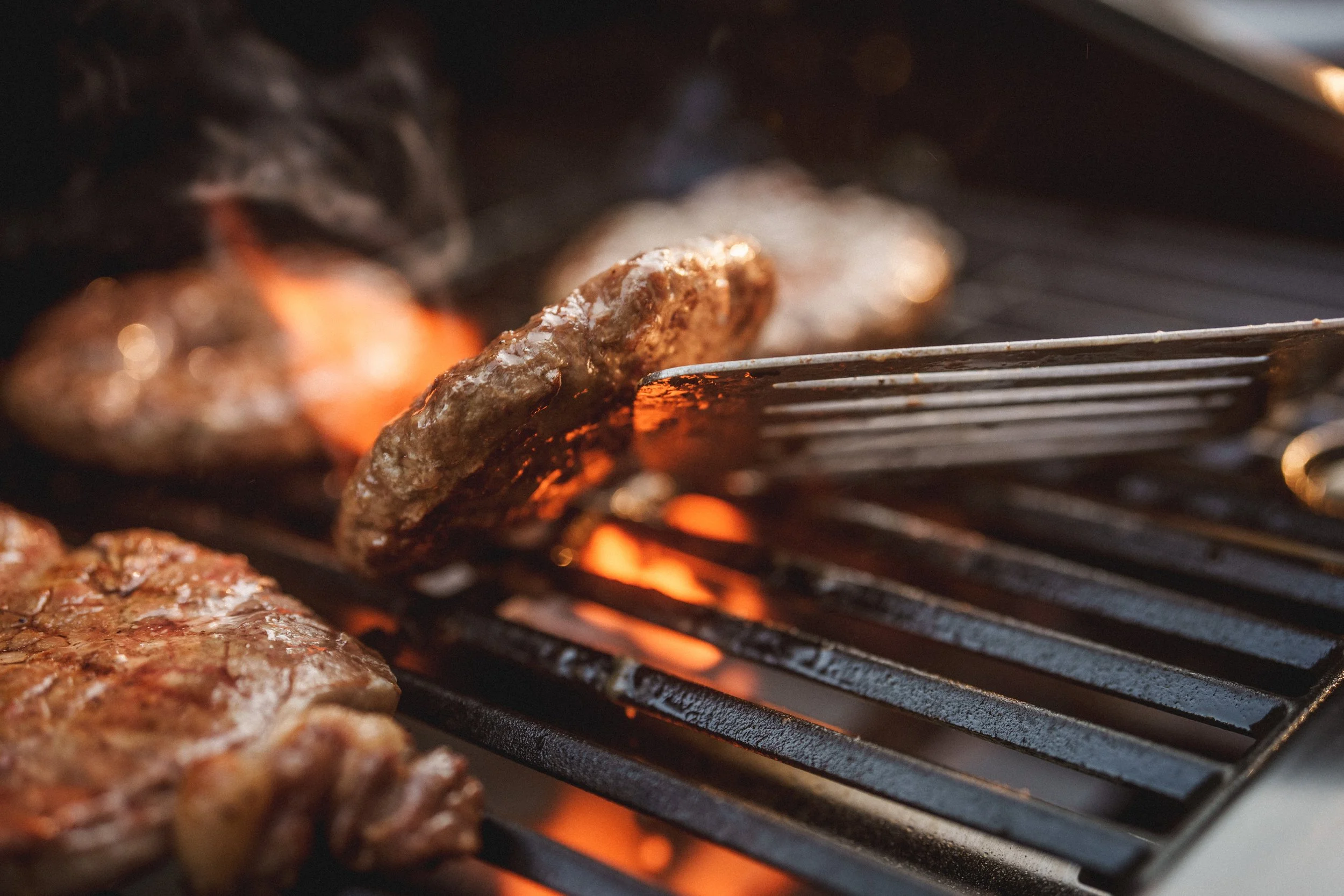 Meat patties cooking on a grill over open flames.