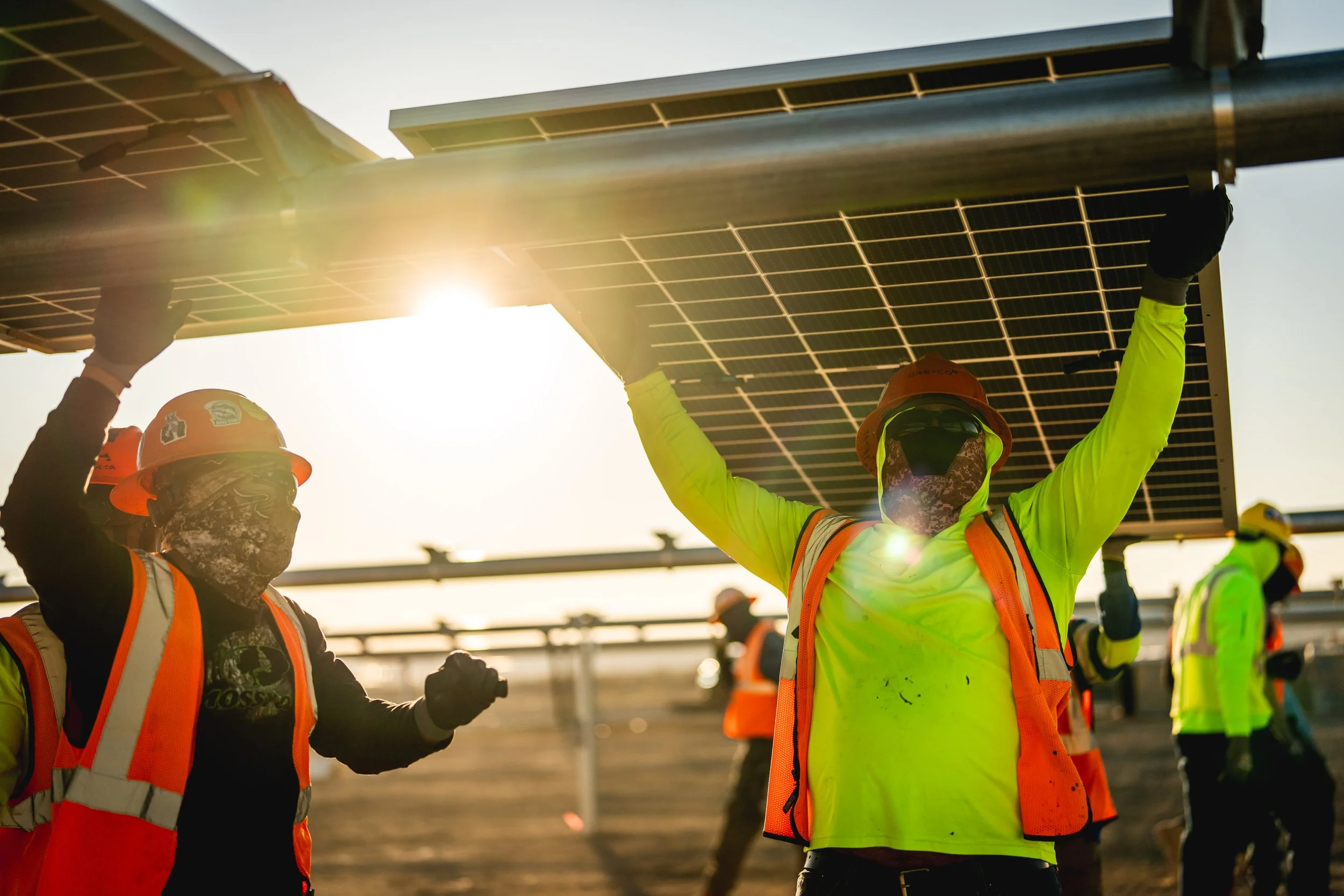 Workers in safety gear installing solar panels on a sunny day.
