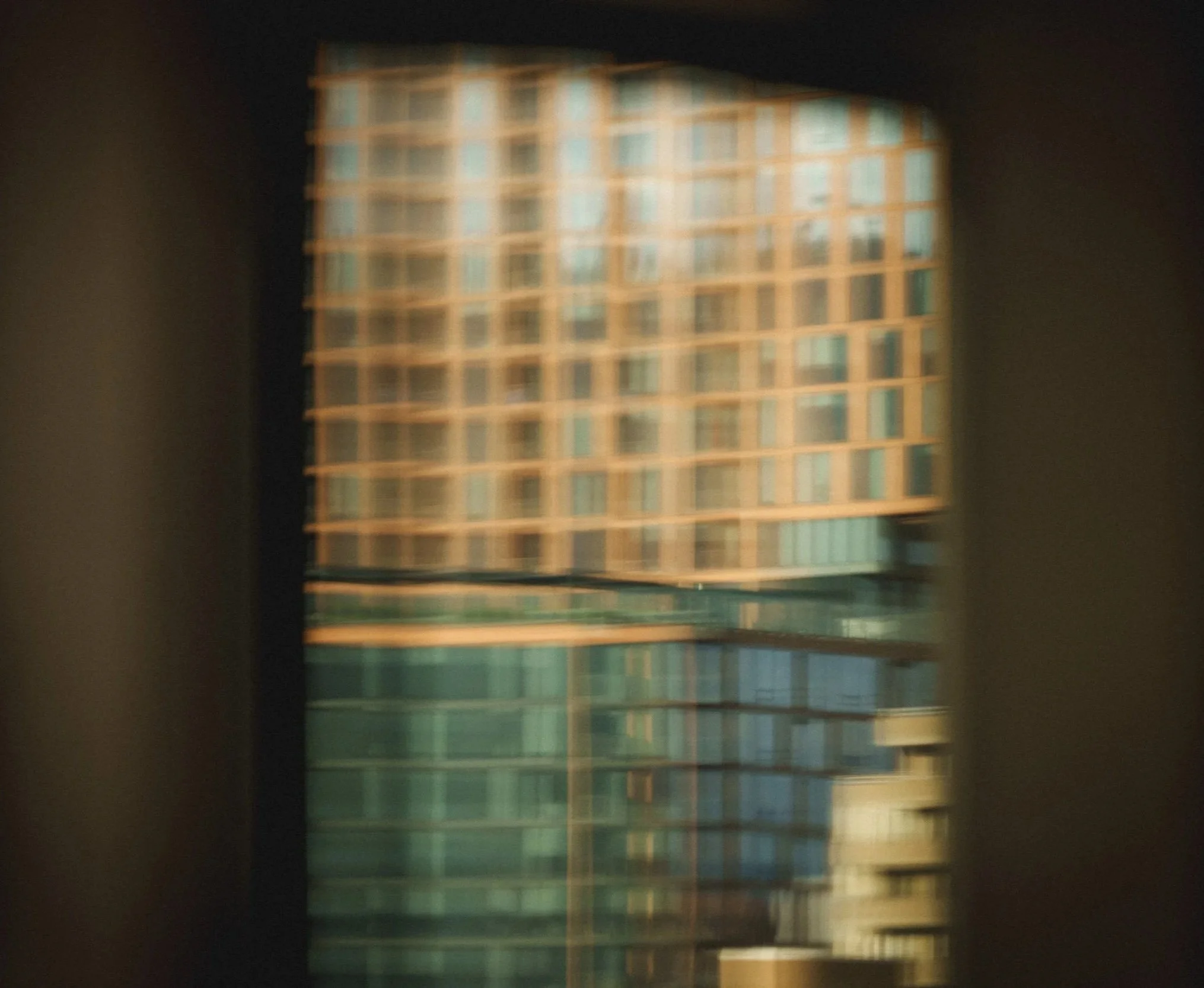 Blurred view of a multi-story building with a grid pattern of windows, seen through a window or opening.