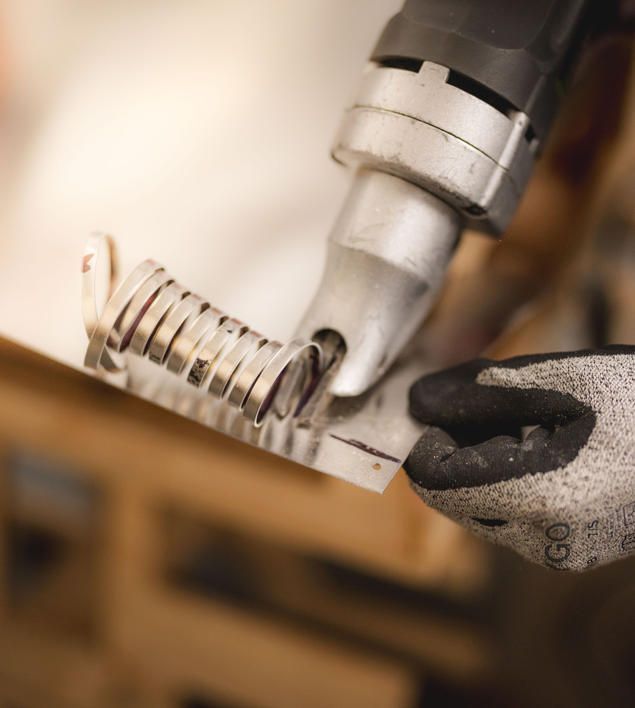 A person wearing black gloves uses a heat gun to straighten a metal spring.