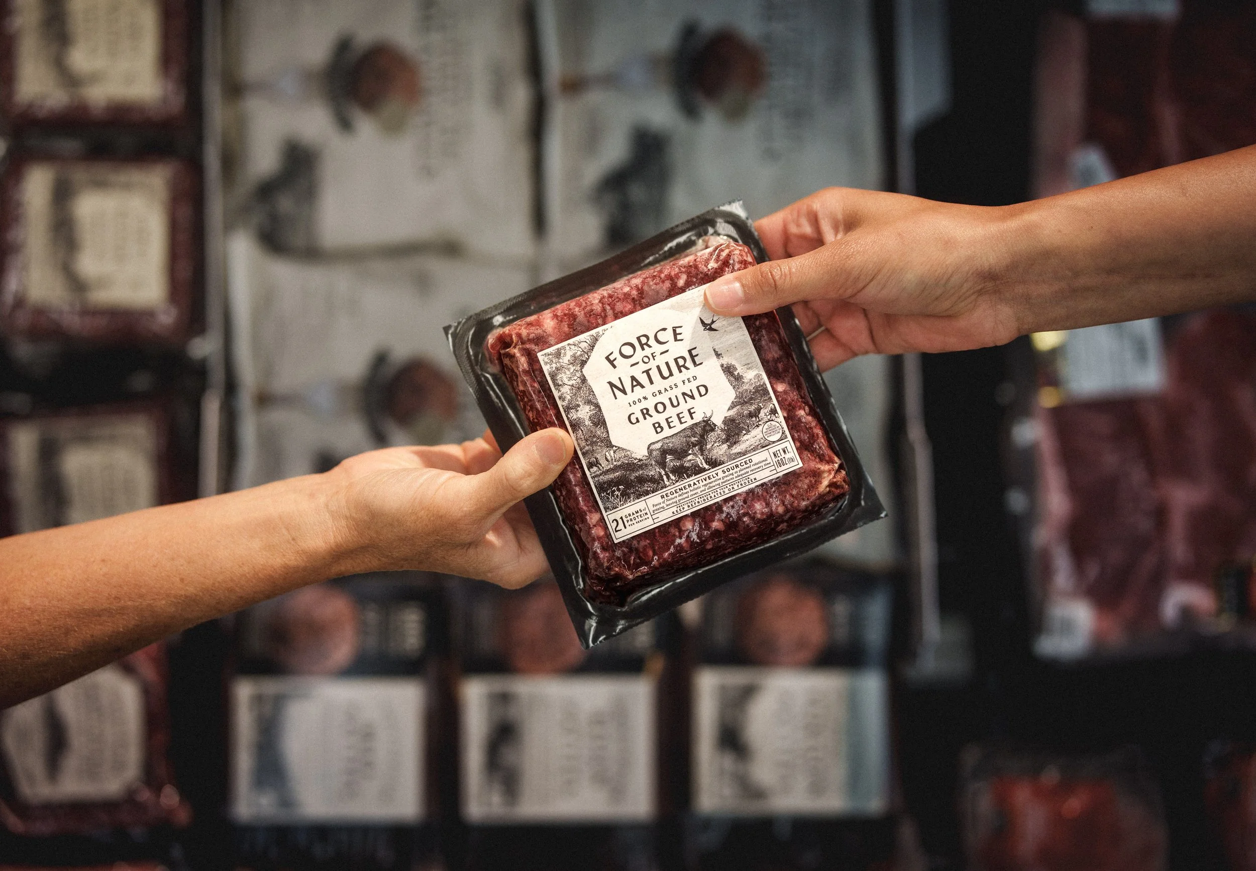 Two hands exchanging a package of ground beef labeled 'Force of Nature' at a grocery store.