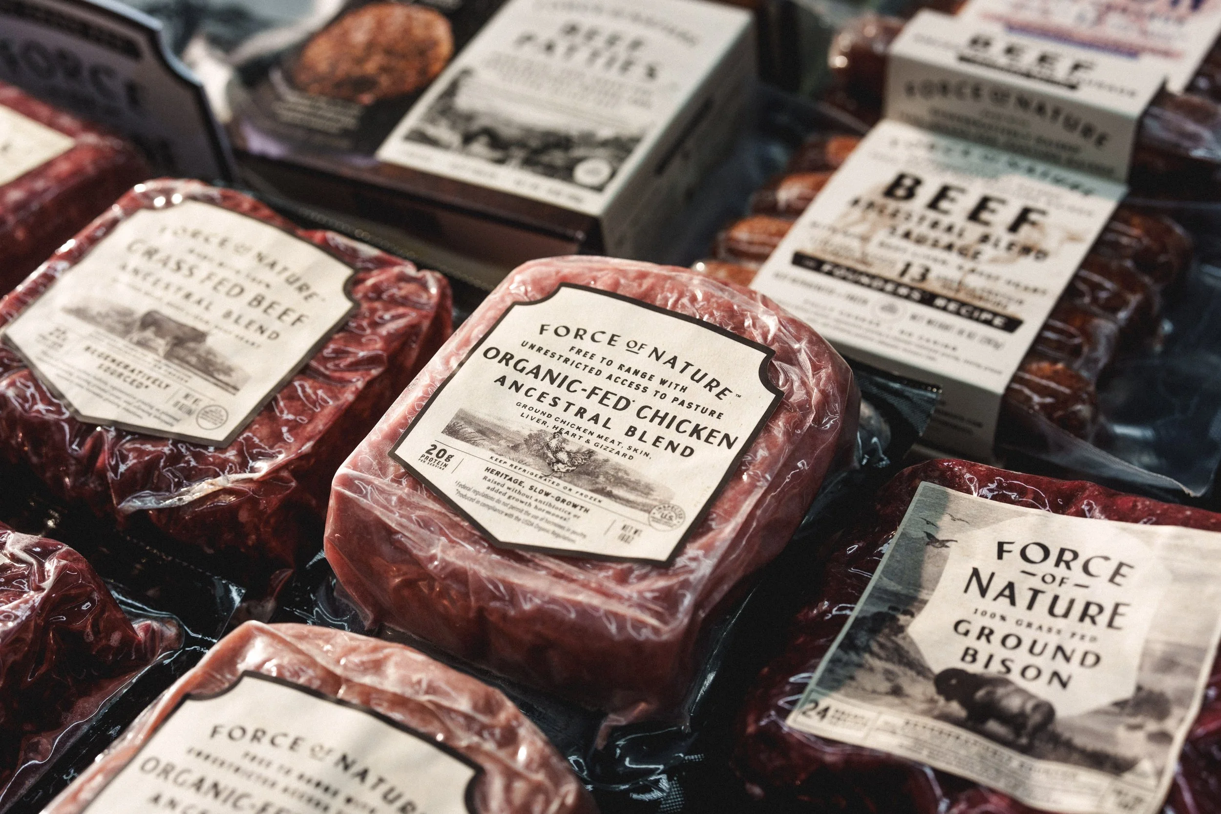 Packages of ground beef and chicken from Force of Nature at a grocery store, with labels indicating organic and ancestral blends.