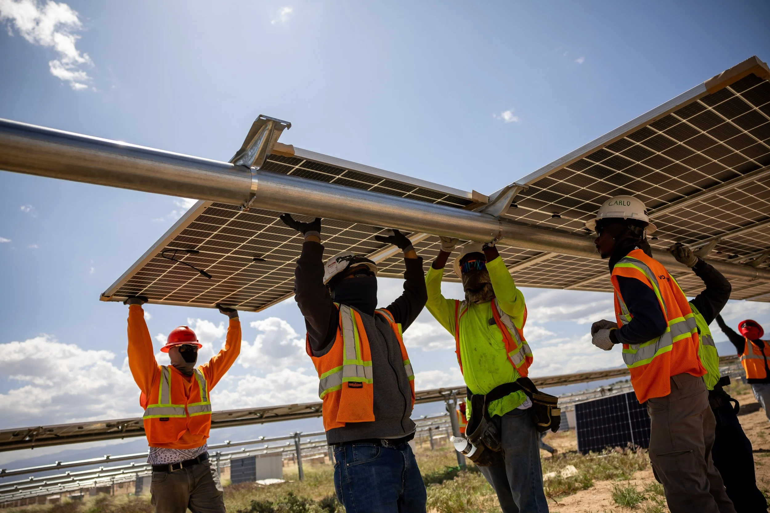 Group of construction workers installing solar panels in a field on a sunny day.