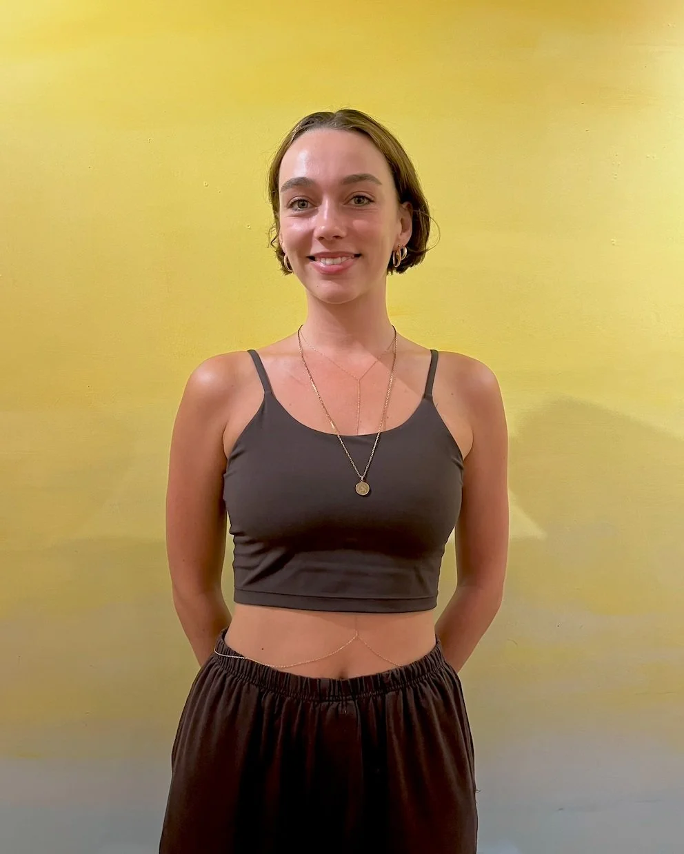 Woman with short hair wearing a dark crop top and skirt, standing against a yellow background.