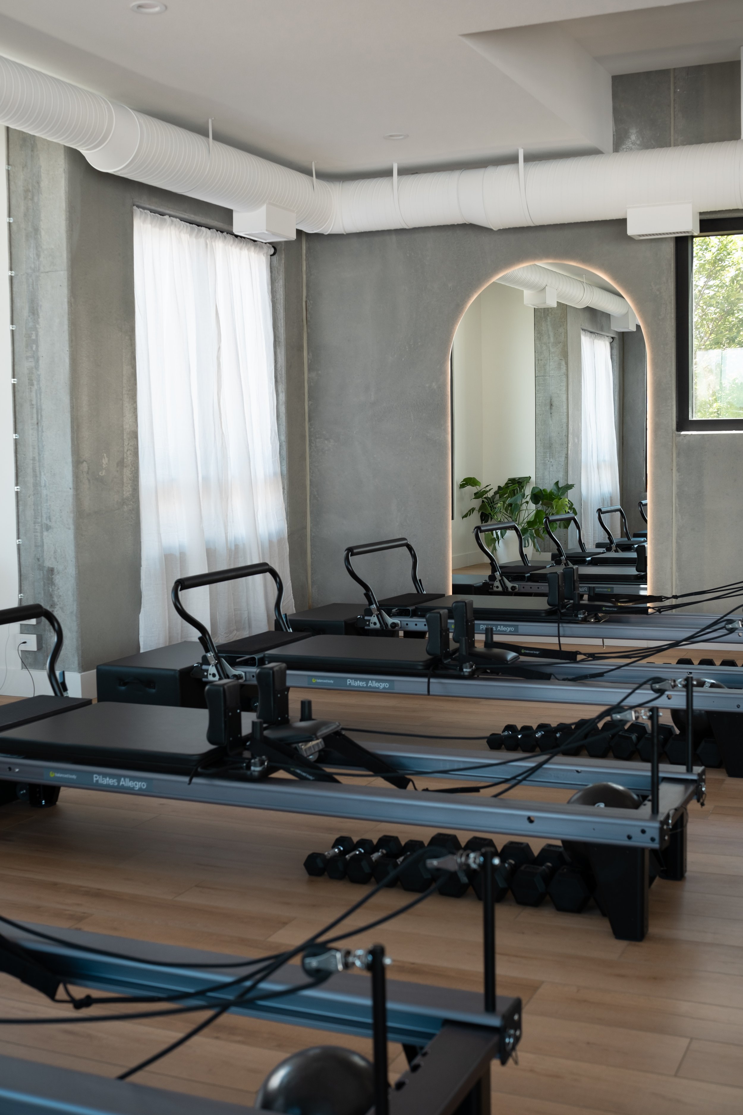 Pilates Allegro reformer machines in a modern fitness studio with natural light, mirror, and plants.