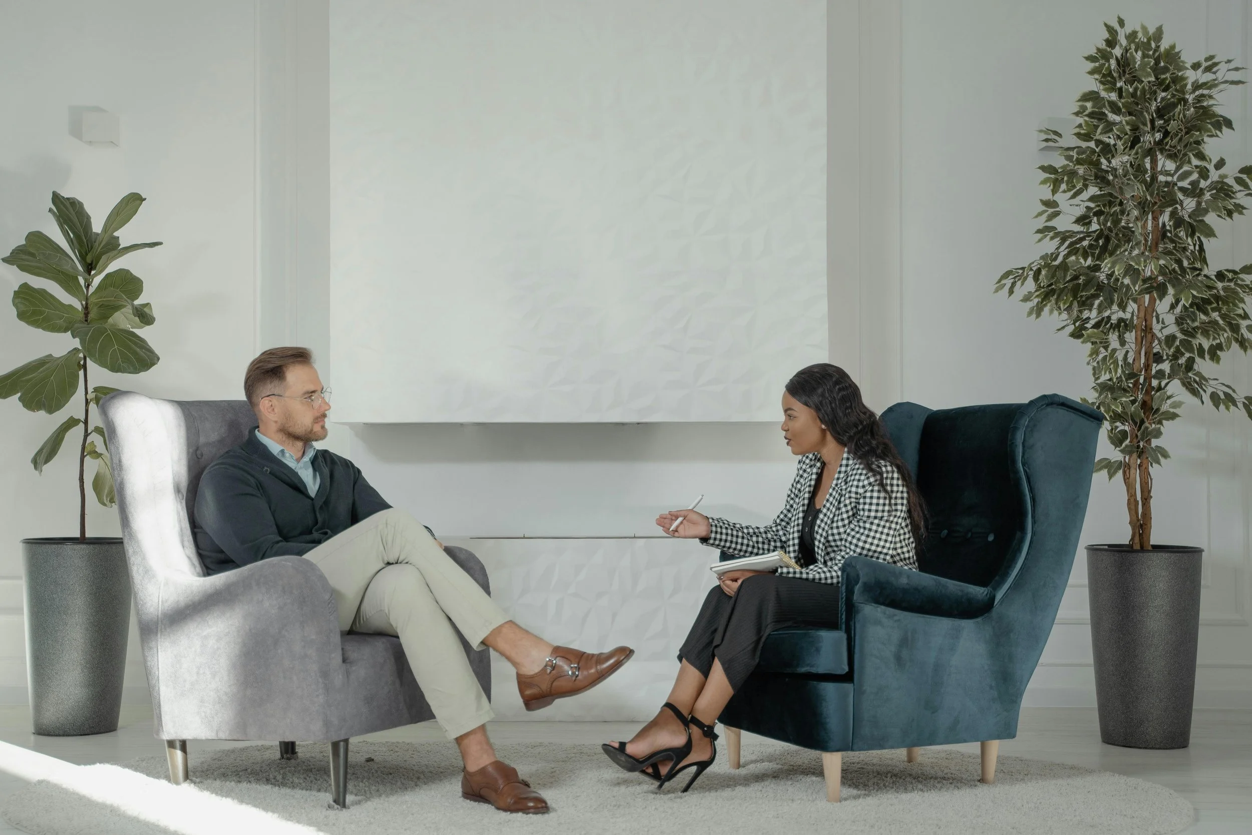 A man and woman seated in chairs, engaged in a trauma therapy session within a softly lit room - Reflection Psychology