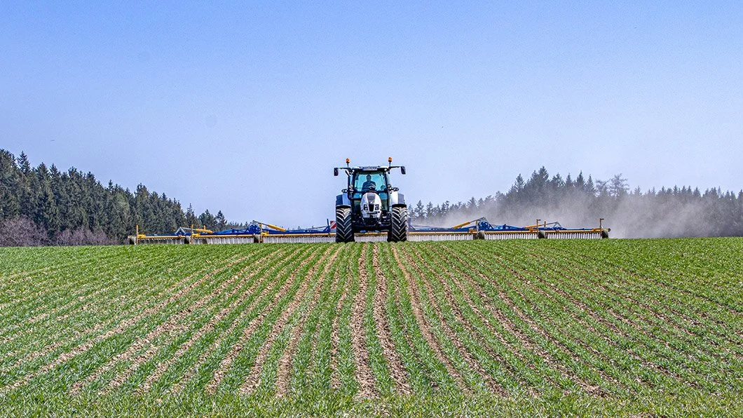 Un tracteur en train de herser un champ de céréales avec une herse étrille treffler