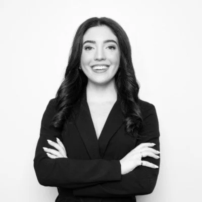 Black and white photo of a smiling woman with long hair in a suit, arms crossed.