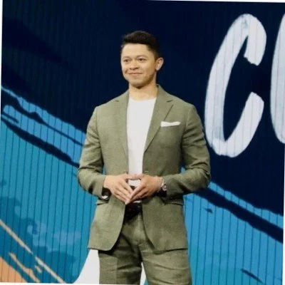 Man in a green suit speaking on stage with a blue background