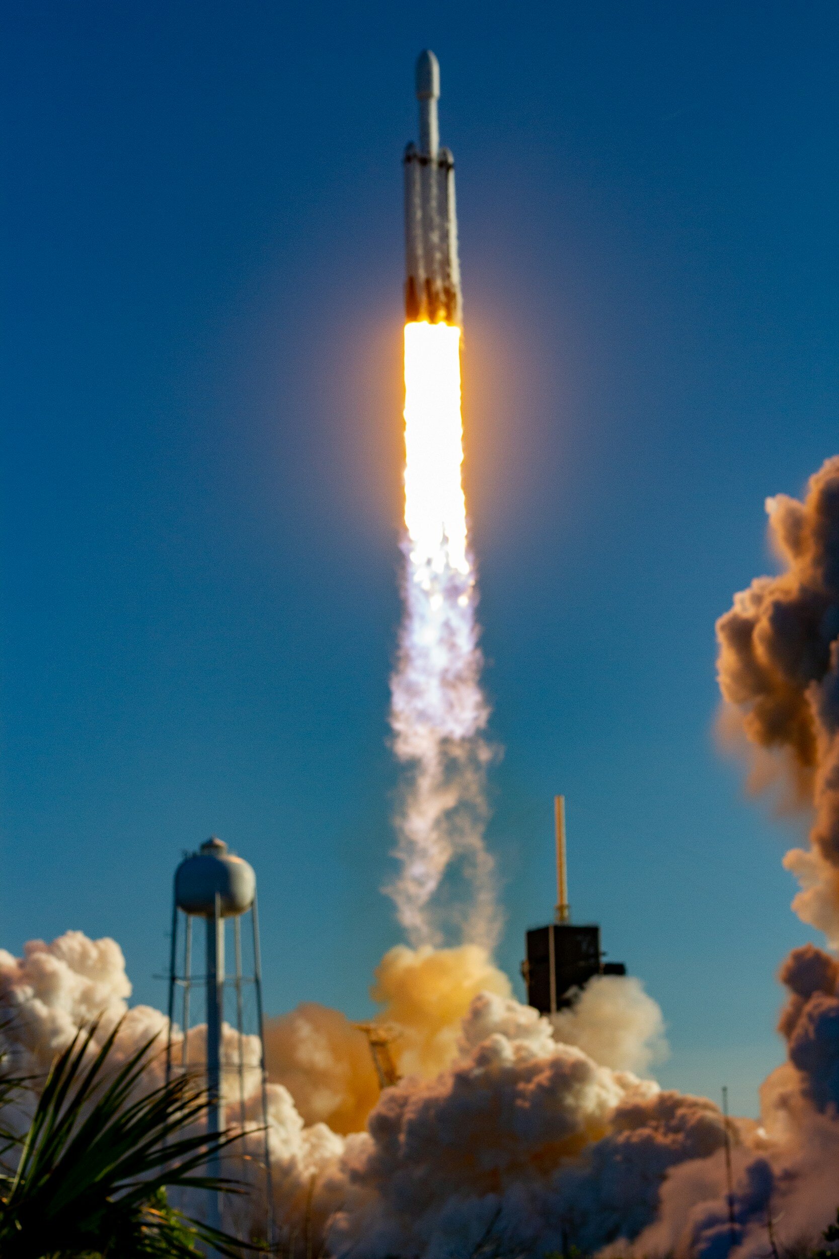 A rocket launching into the sky with flames and smoke at its base, several clouds and structures visible in the foreground.
