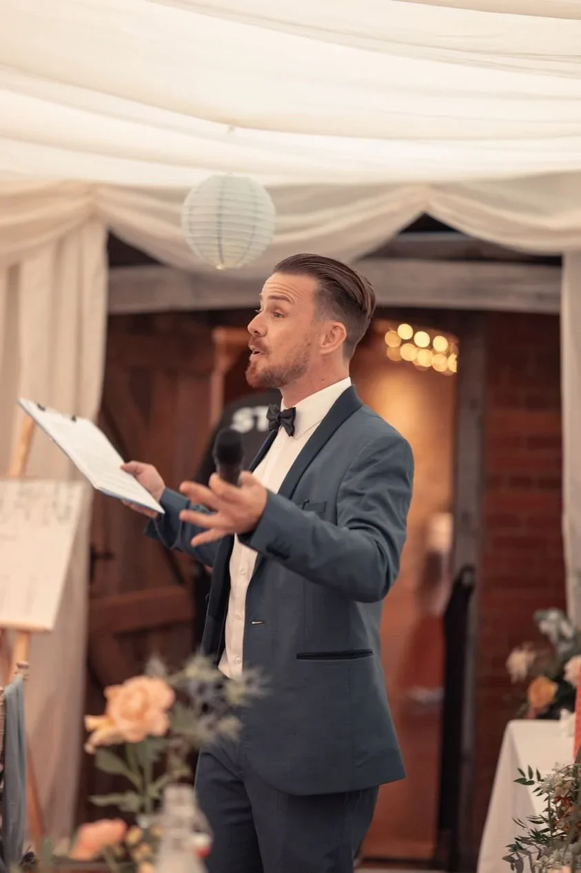 Saul holding a microphone and notes while hosting a wedding