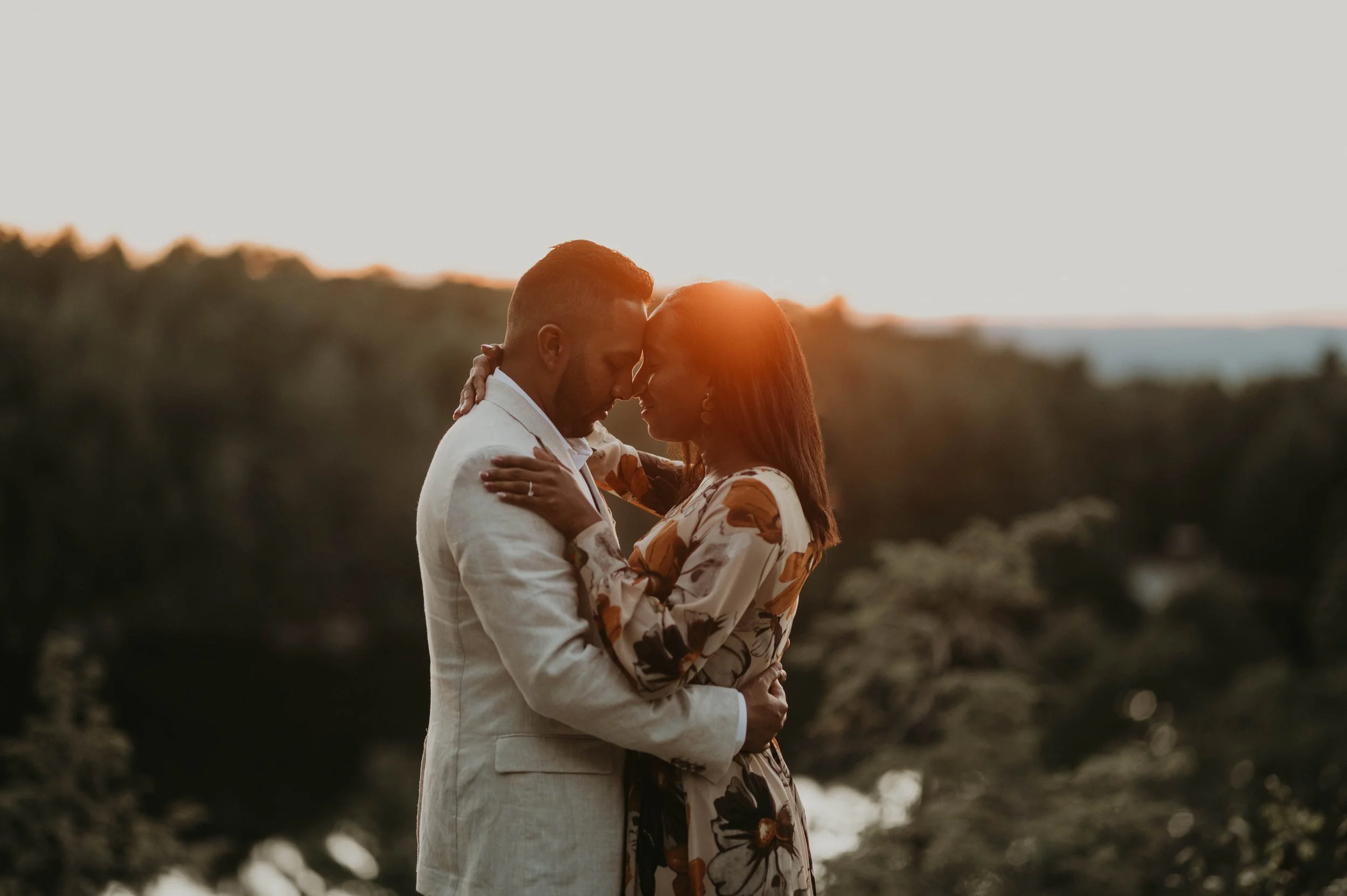 A couple dressed in formal attire embracing during sunset outdoors.