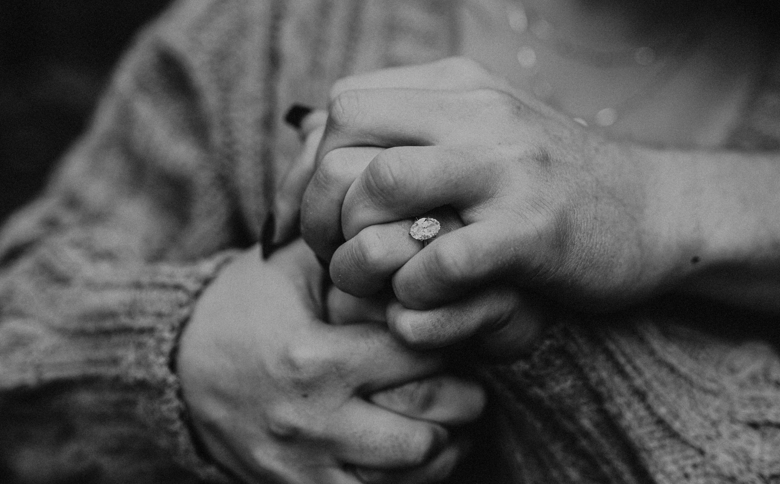 Close-up of two hands clasped, with one hand wearing a ring, in black and white.