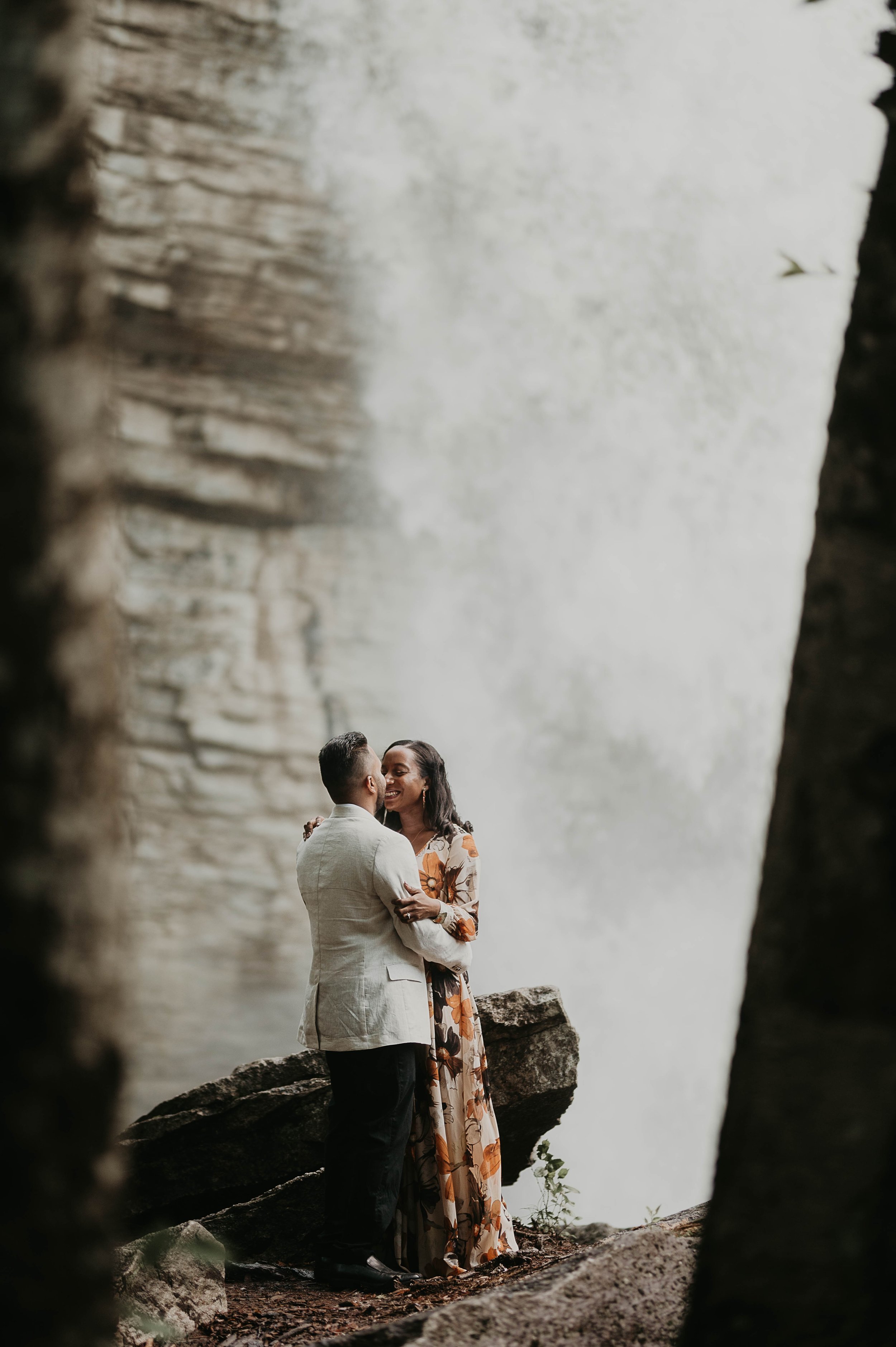 A couple in formal attire sharing a kiss near a waterfall.
