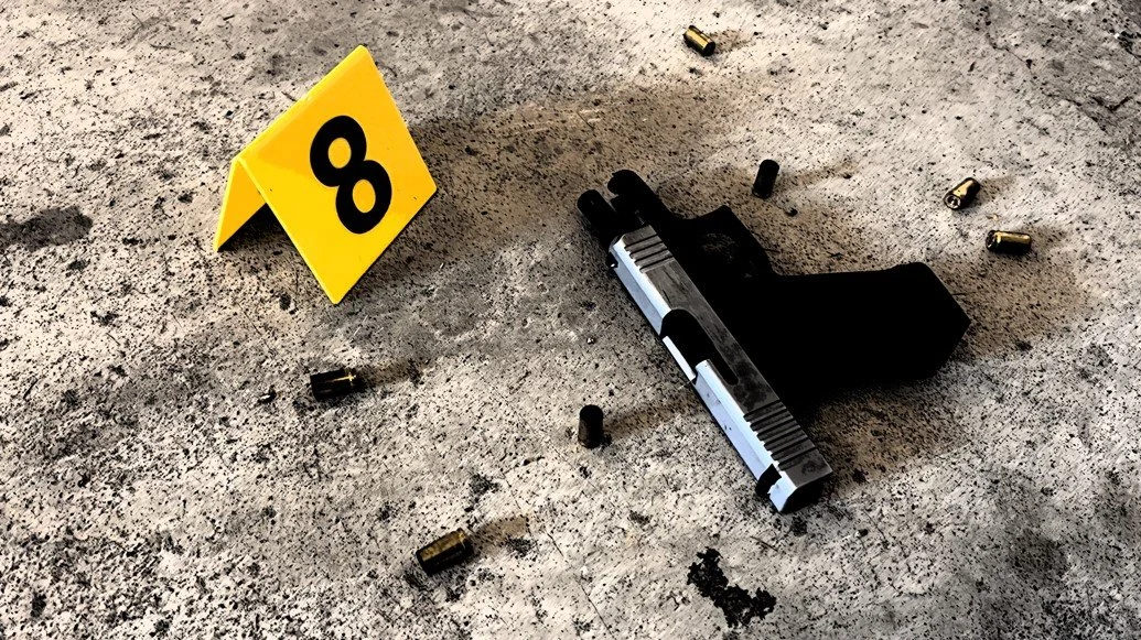 Fired handgun lying on ground surrounded by multiple expended cartridge casings and evidence marker "8".