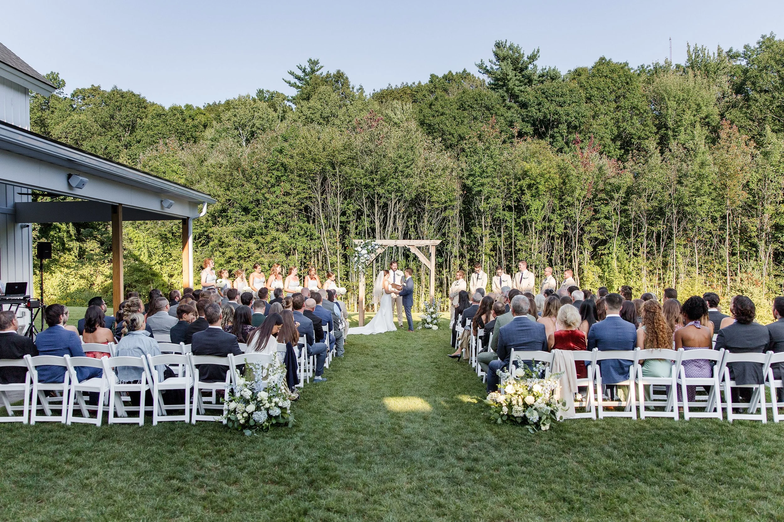 View of wedding ceremony on the Middle Lawn from behind guest seating facing the back woods. 