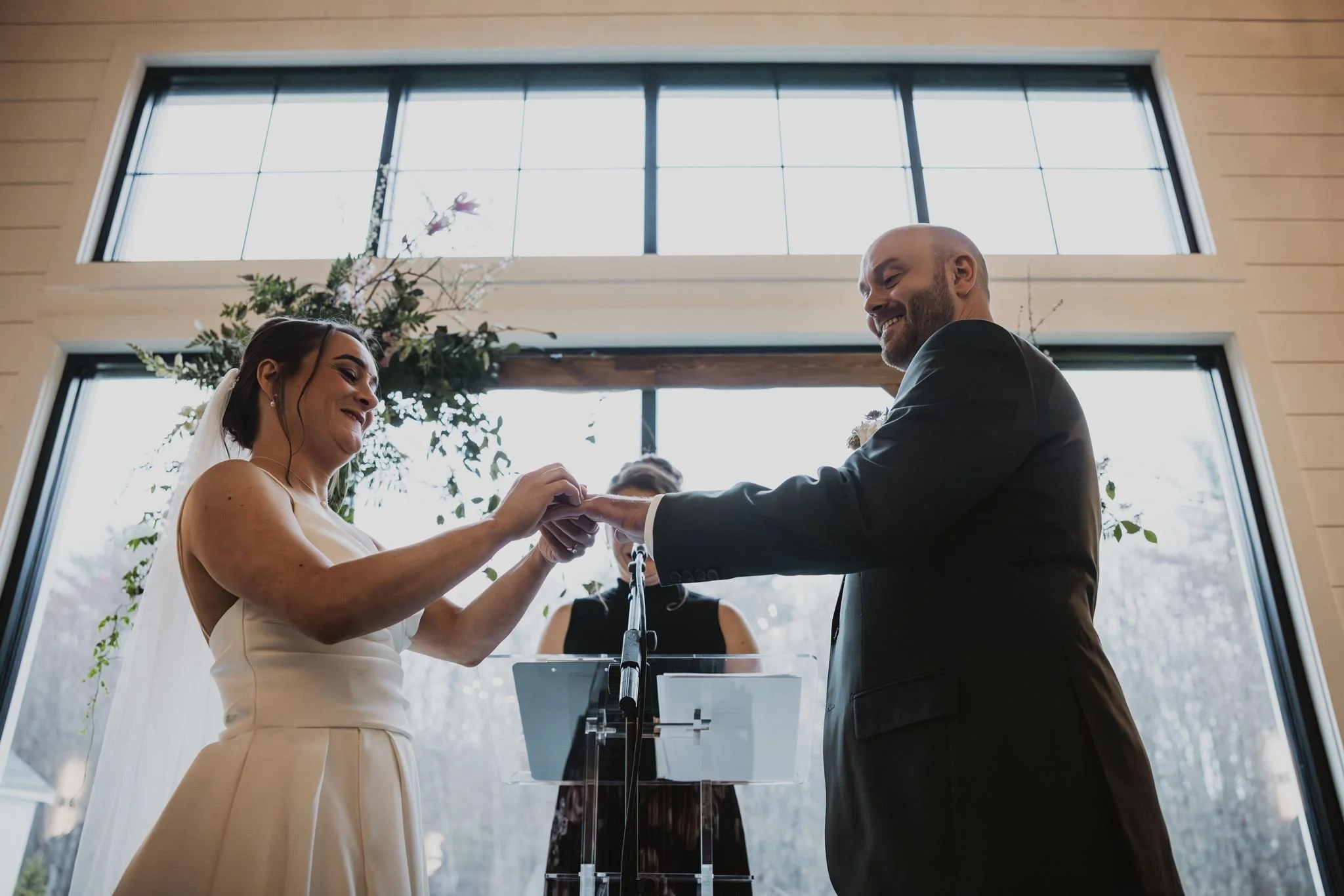 Couple placing rings on each other’s fingers in front of our back windows. 