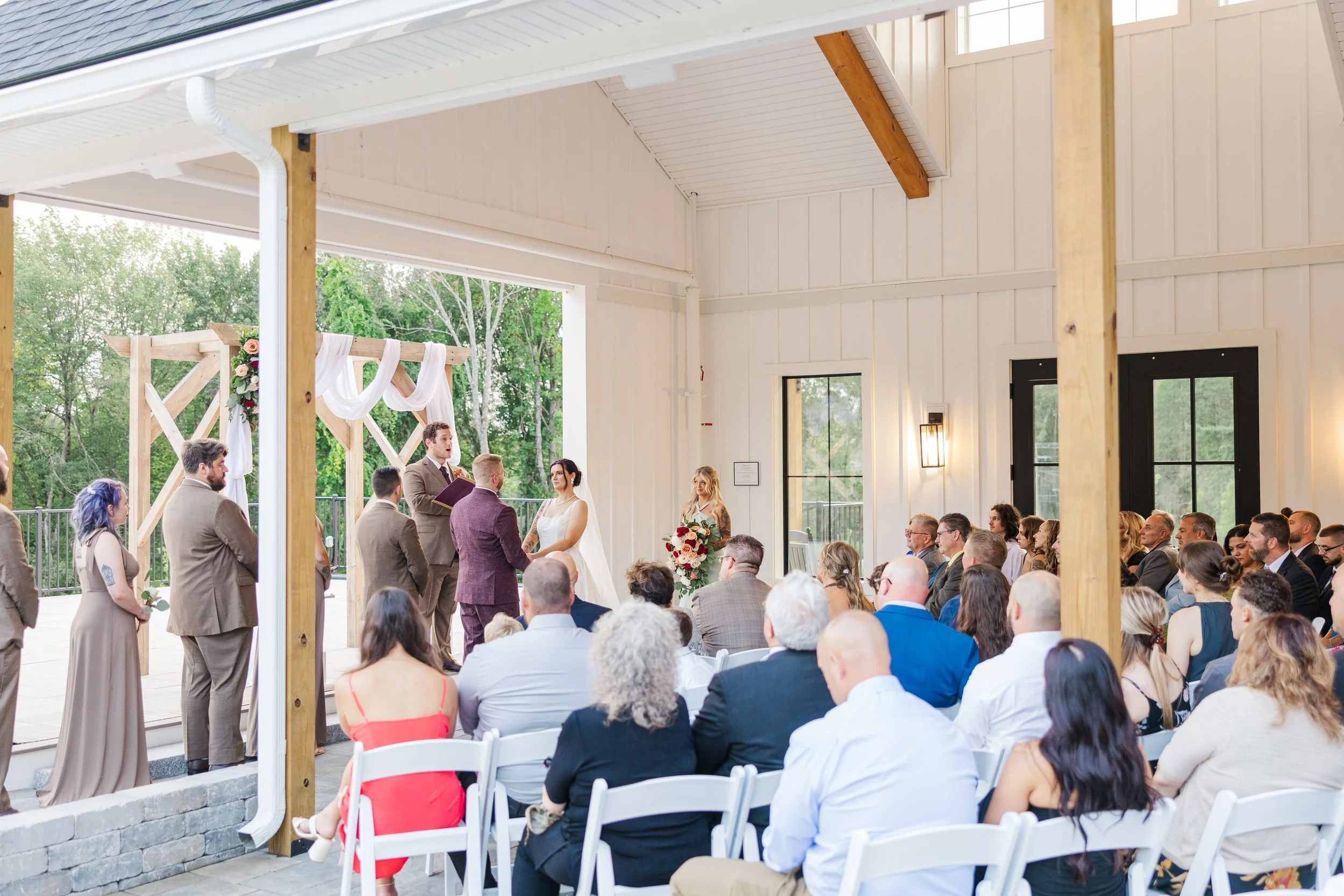 View of wedding ceremony under the Covered Breezeway from back left guest seating outside of covered roof. 