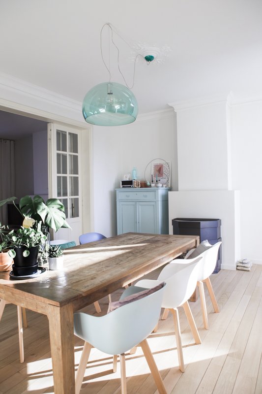  La salle à manger est très lumineuse et la table en bois contraste avec les chaises About a chair de la marque design scandinave Hay. Lampe bleue transparente Kartell.  