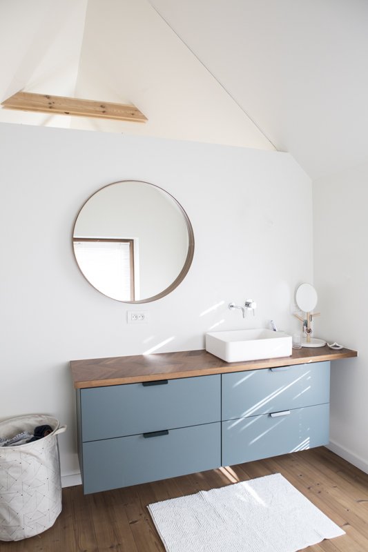  Salle de bain minimaliste et d’inspiration scandinave avec son meuble bleu gris et son grand miroir arrondi.  