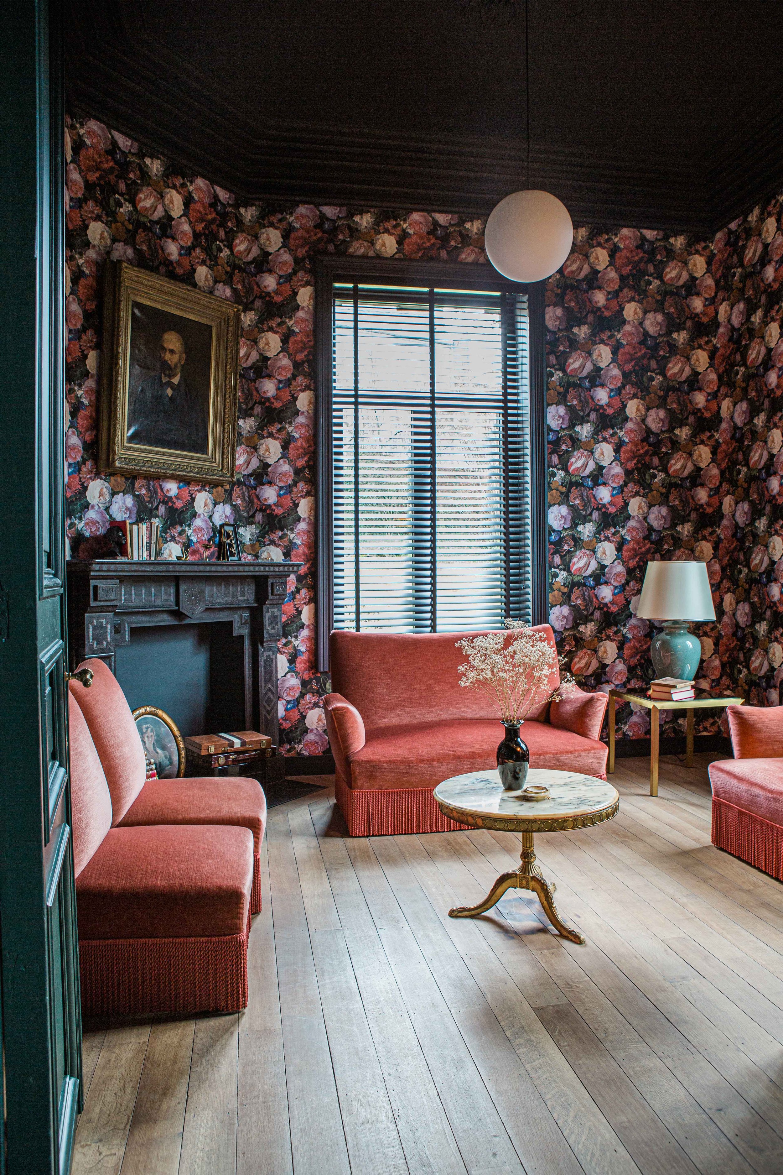 Salon cosy de style vintage et baroque dans les tons rouge et orange dans laquelle on retrouve un papier-peint fleuri et une table basse en marbre chinée  