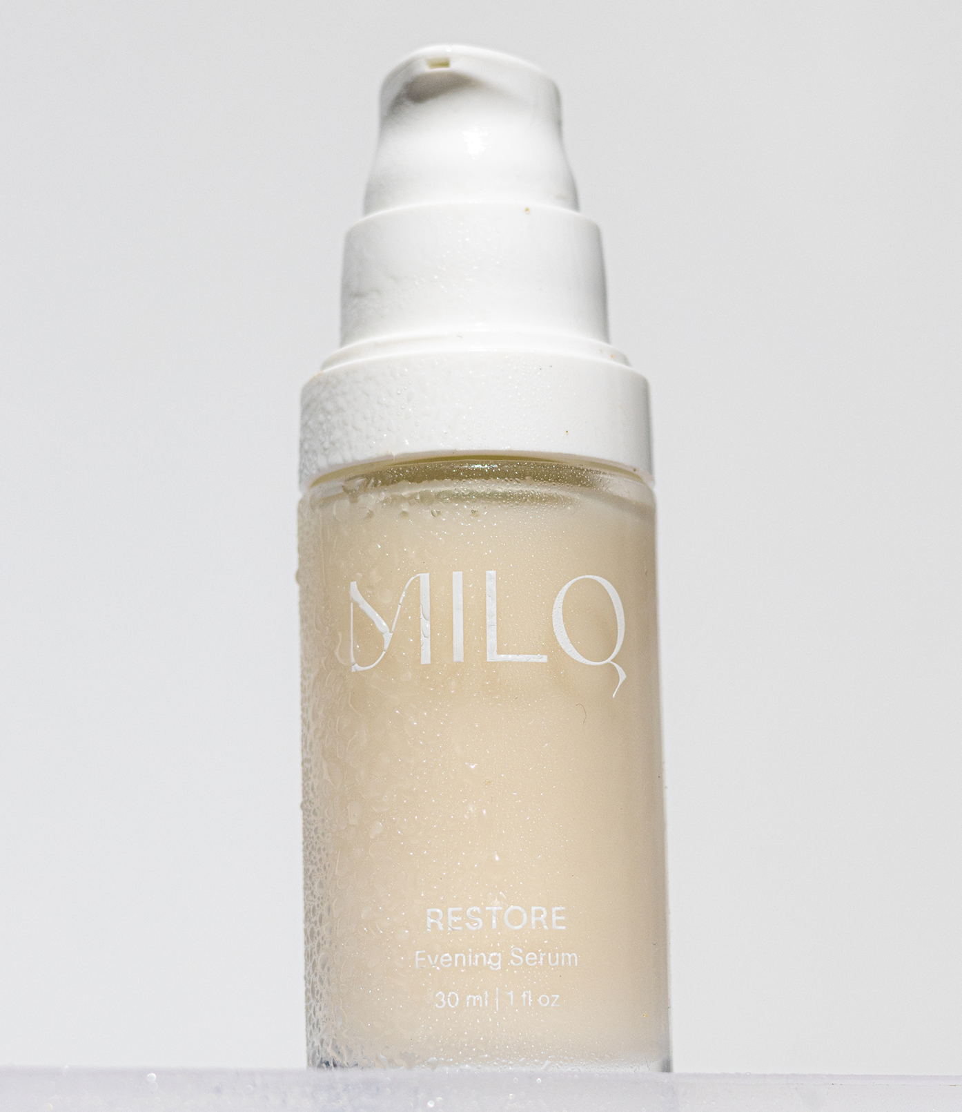 A clear bottle of milo Restore Evening Serum with condensation on the outside, a white pump dispenser top, and minimalistic white label text.