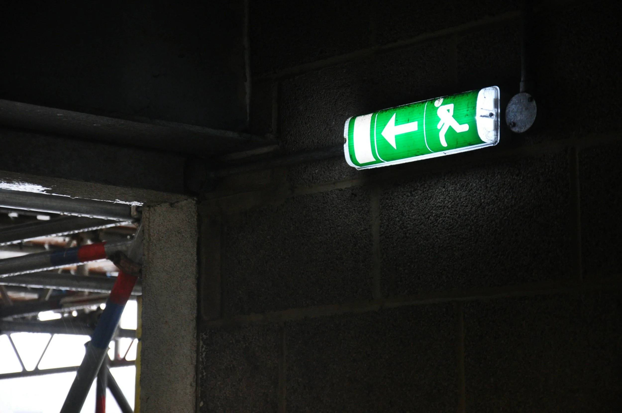 Green emergency exit sign with a left arrow and running figure, mounted on a dark wall in a building