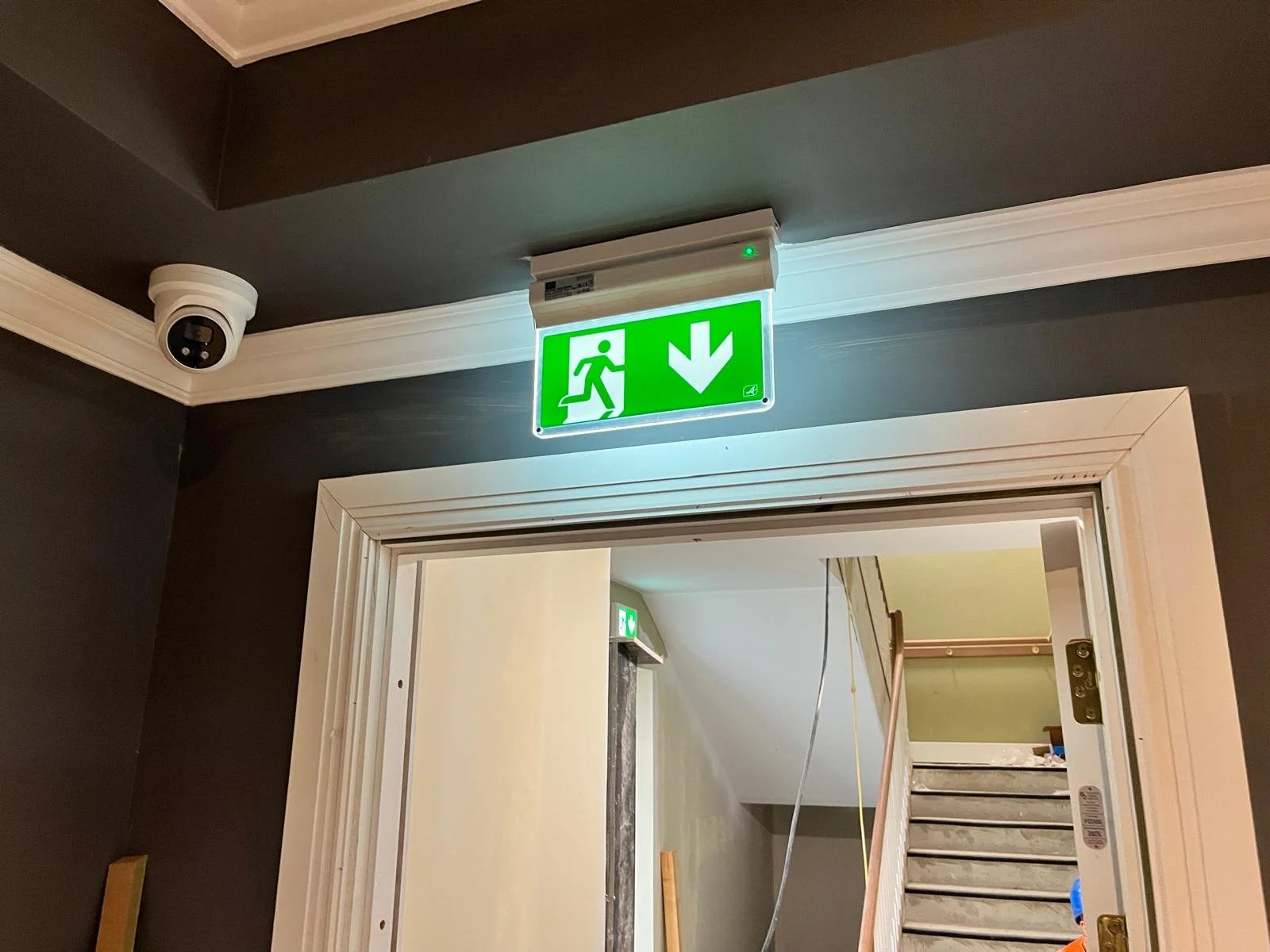 Green and white emergency exit sign with running figure and downward arrow, mounted above a doorway.