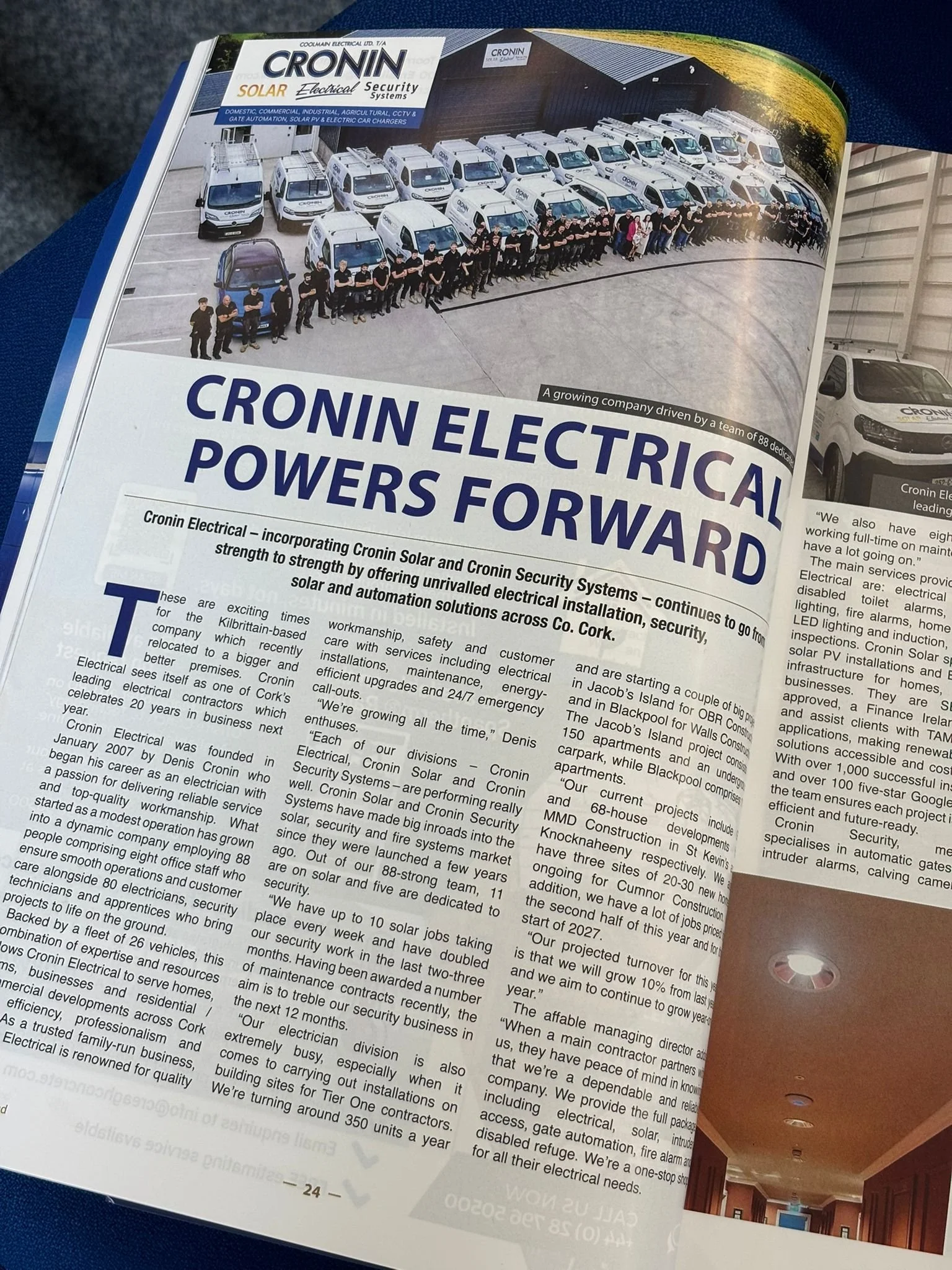 A magazine open to an advertisement for Cronin Electrical, showing a group of employees standing in front of company vehicles in an industrial parking lot. The article discusses the company's electrical and security systems services.