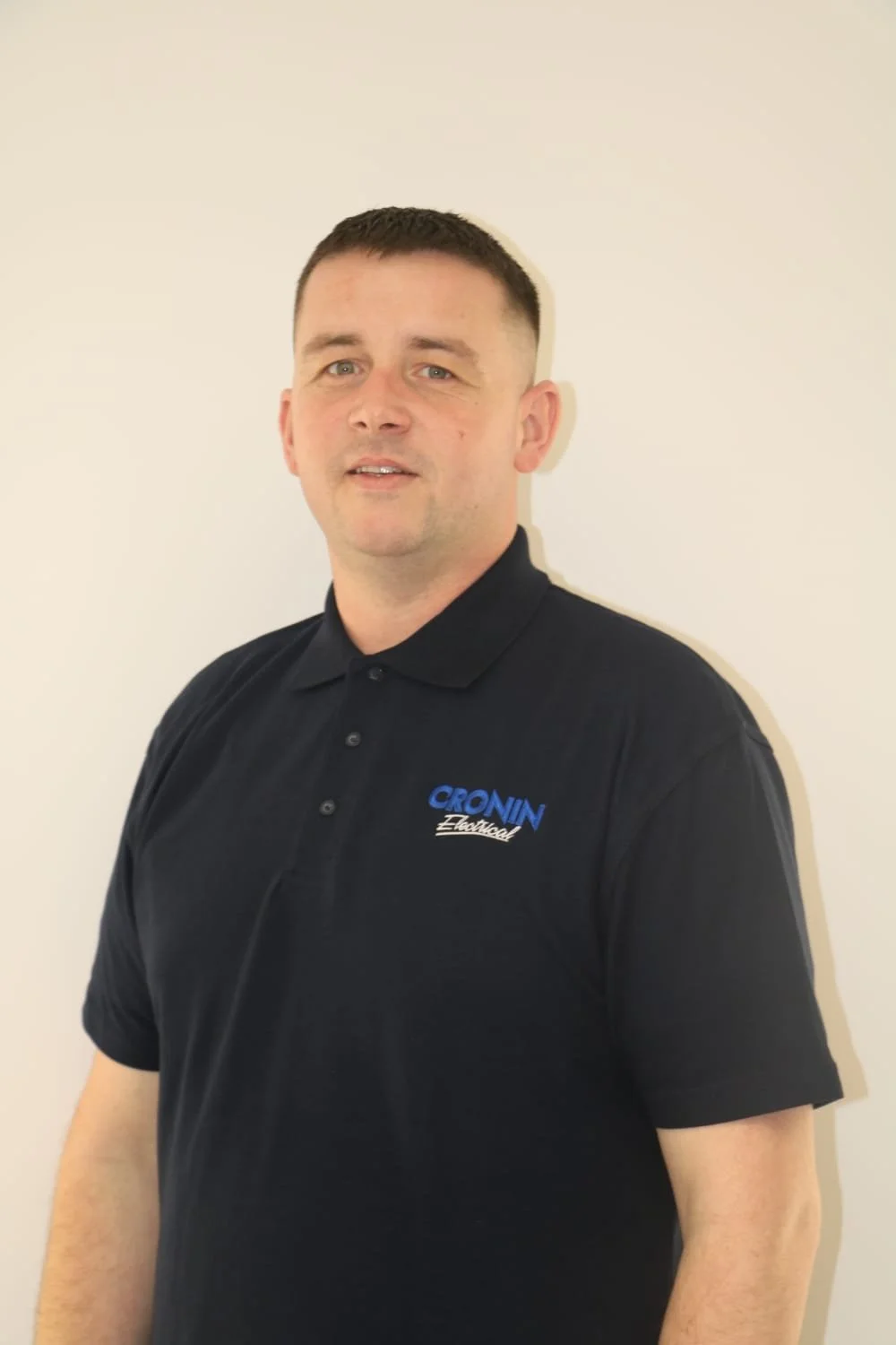 A man with short dark hair wearing a black polo shirt with a logo that reads 'CROVIN Electrical' stands against a plain white wall.