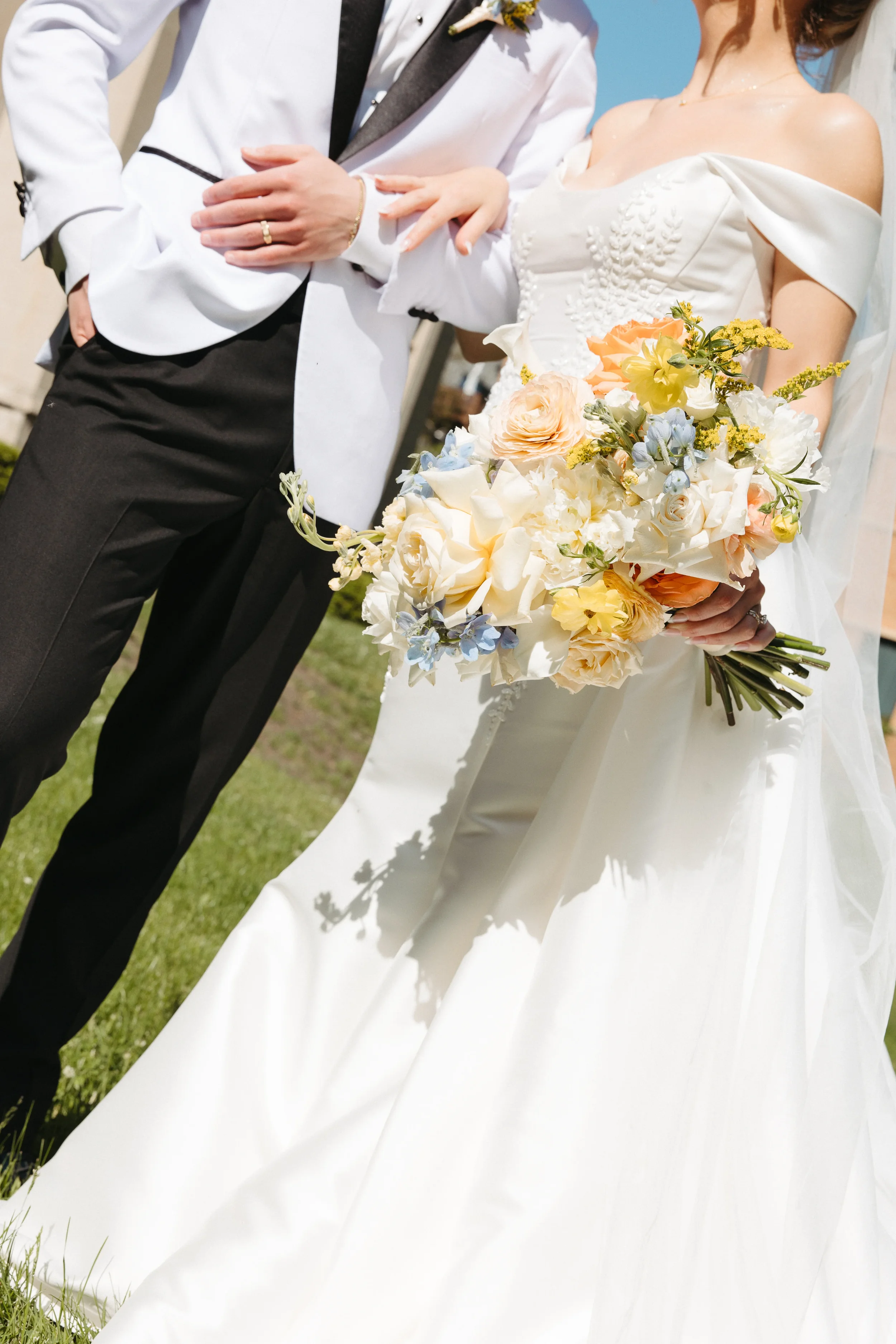 Close-up of a bride holding a bouquet of flowers and a groom standing beside her at an outdoor wedding.