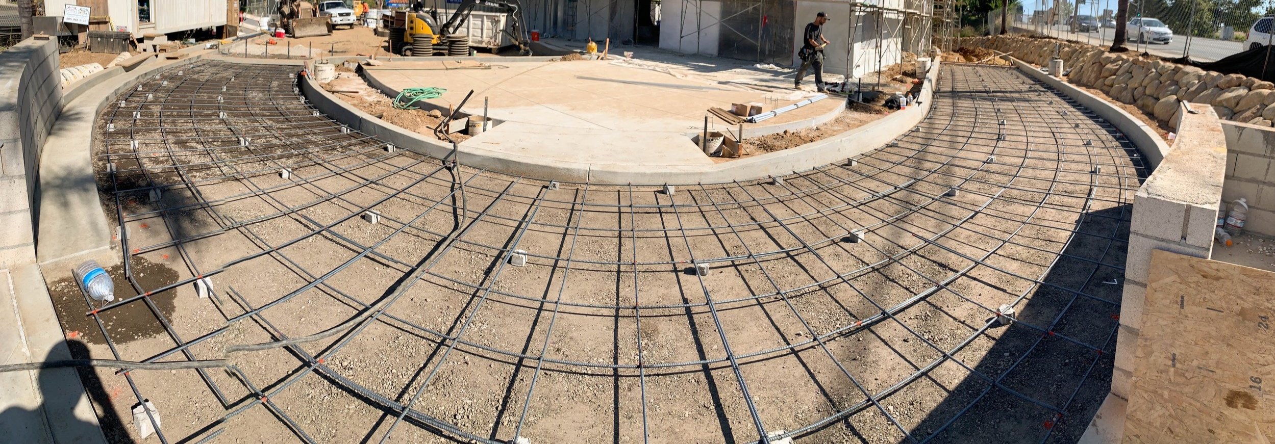 Construction site with circular foundation layout, rebar grid, and workers.