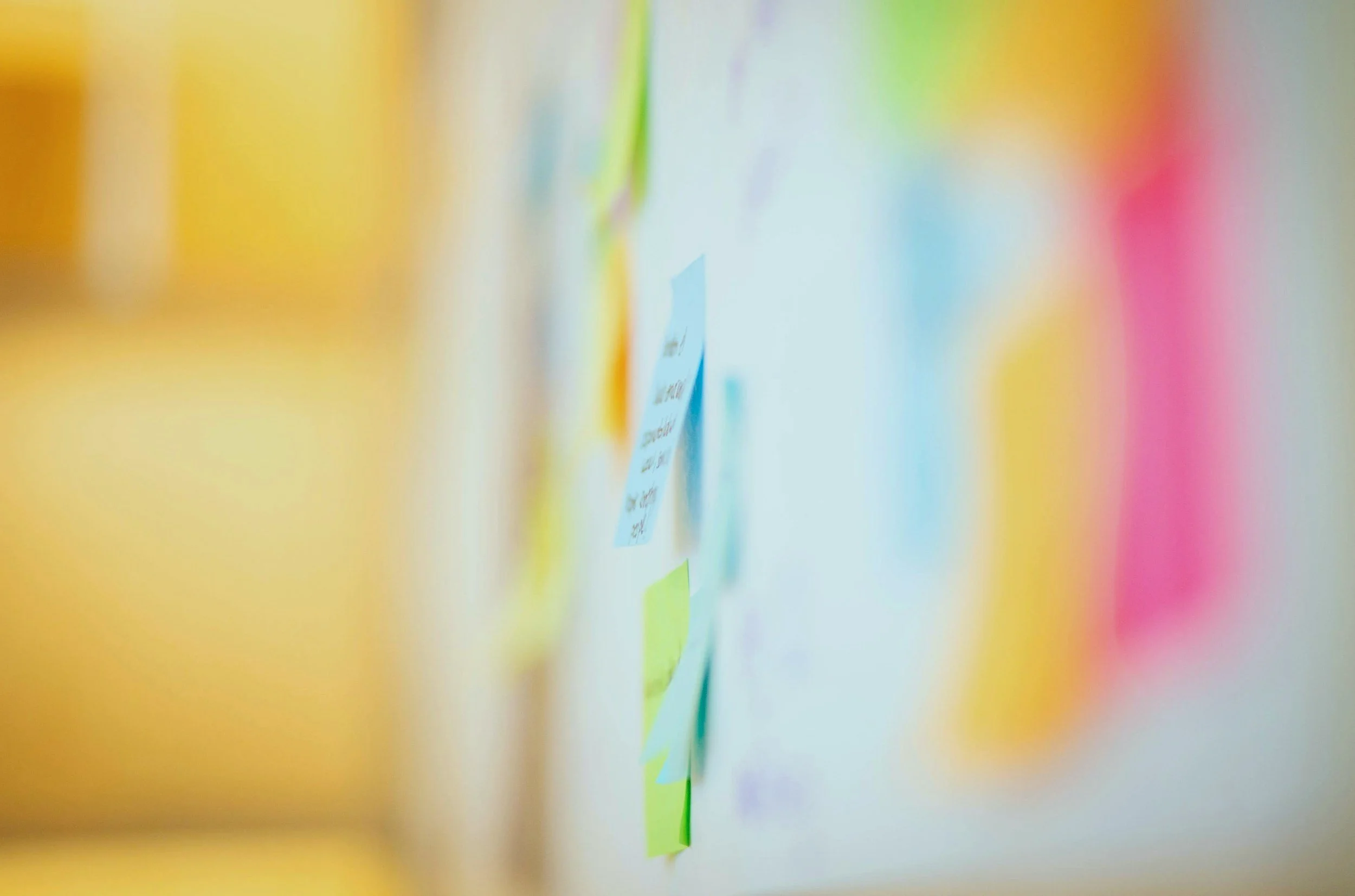 Blurred image of colorful sticky notes or papers on a white wall or board.