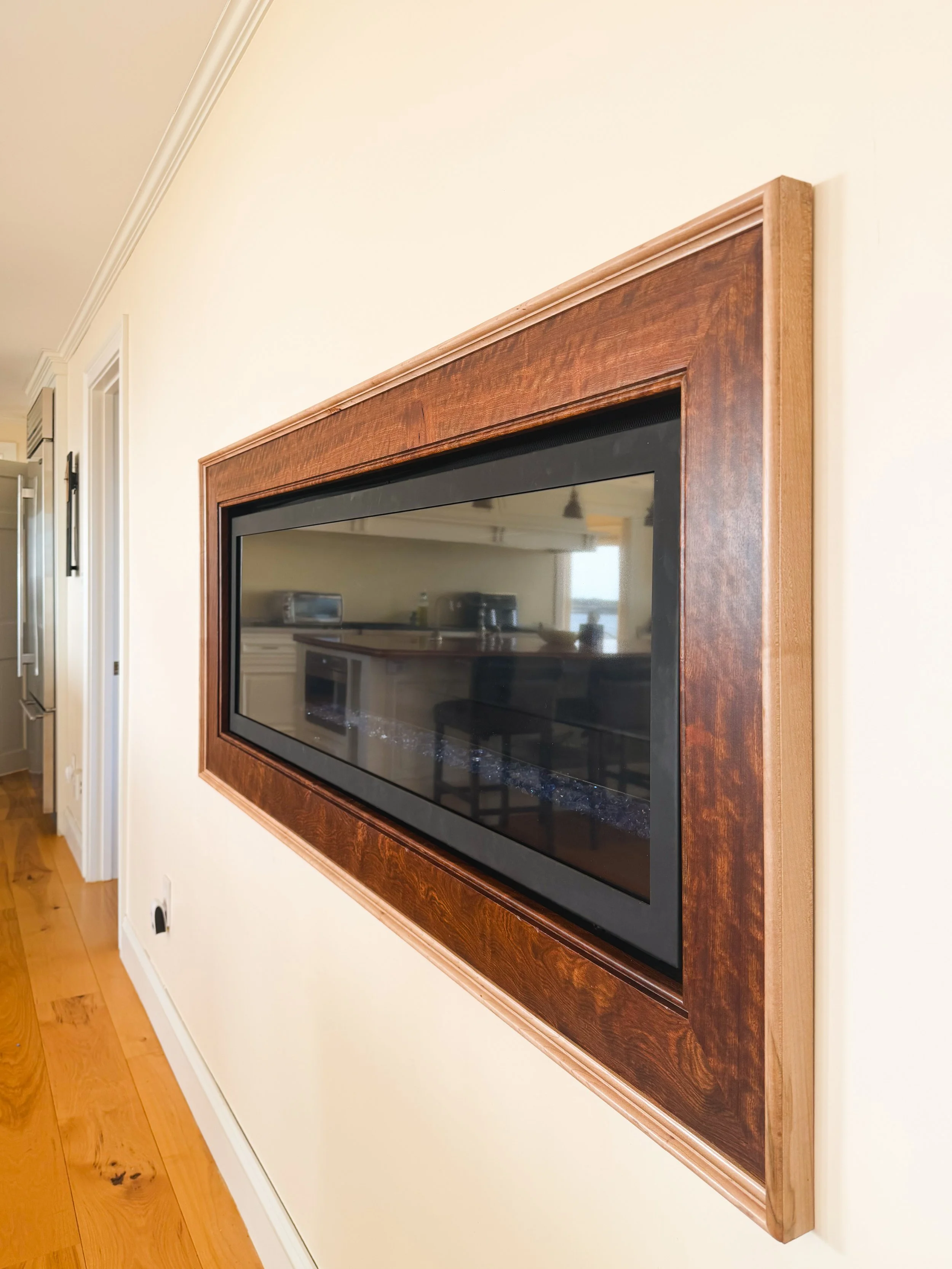 Flat-screen television mounted on a wall in a home, surrounded by a wooden frame.