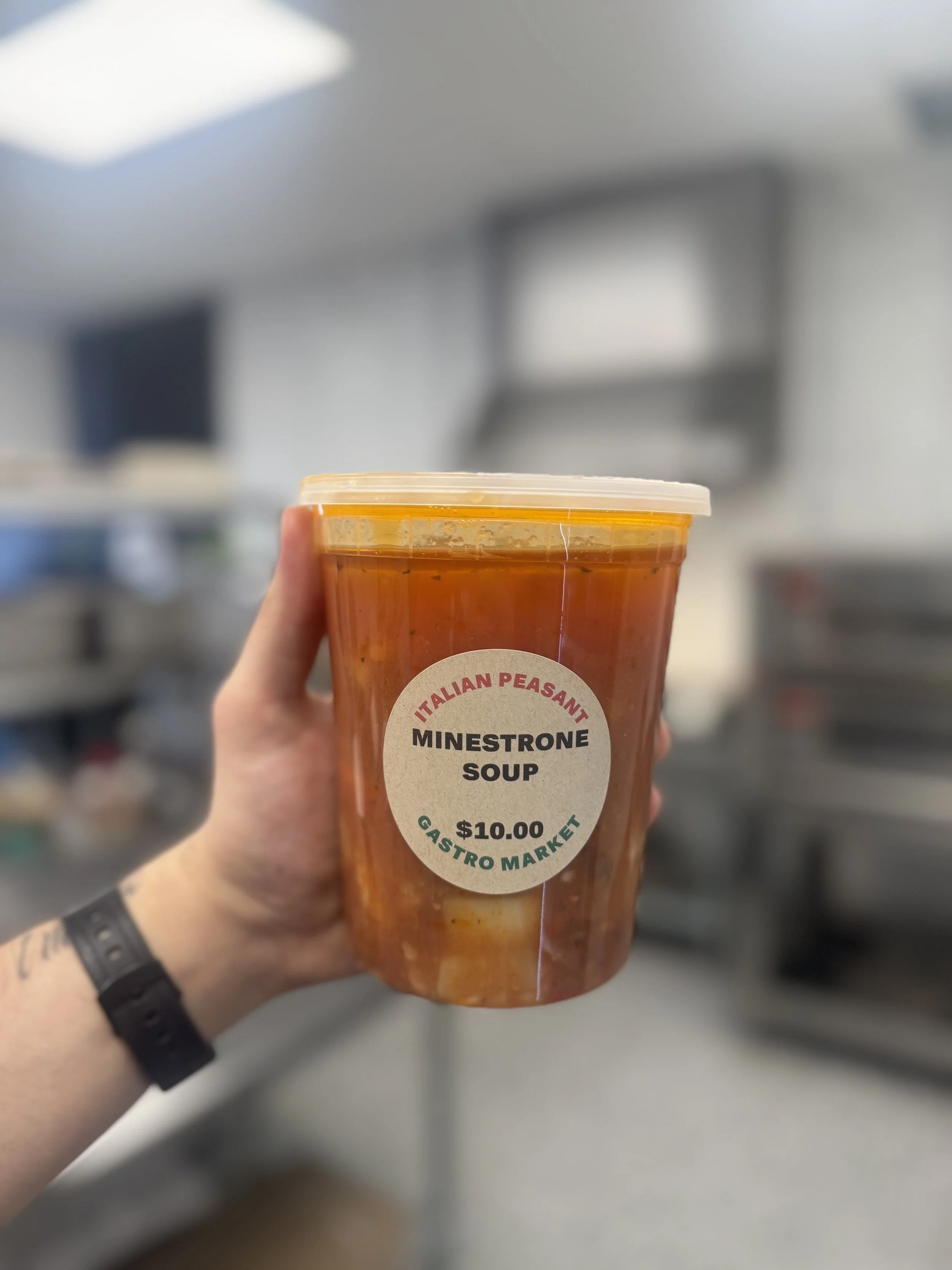 A hand holding a container of Minestrone soup in a kitchen setting.