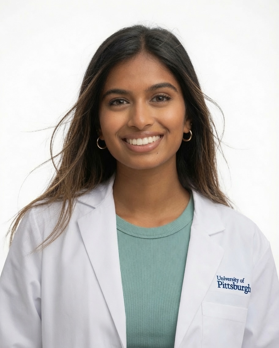 Woman smiling in a professional headshot wearing a white medical coat and green top against a light background.