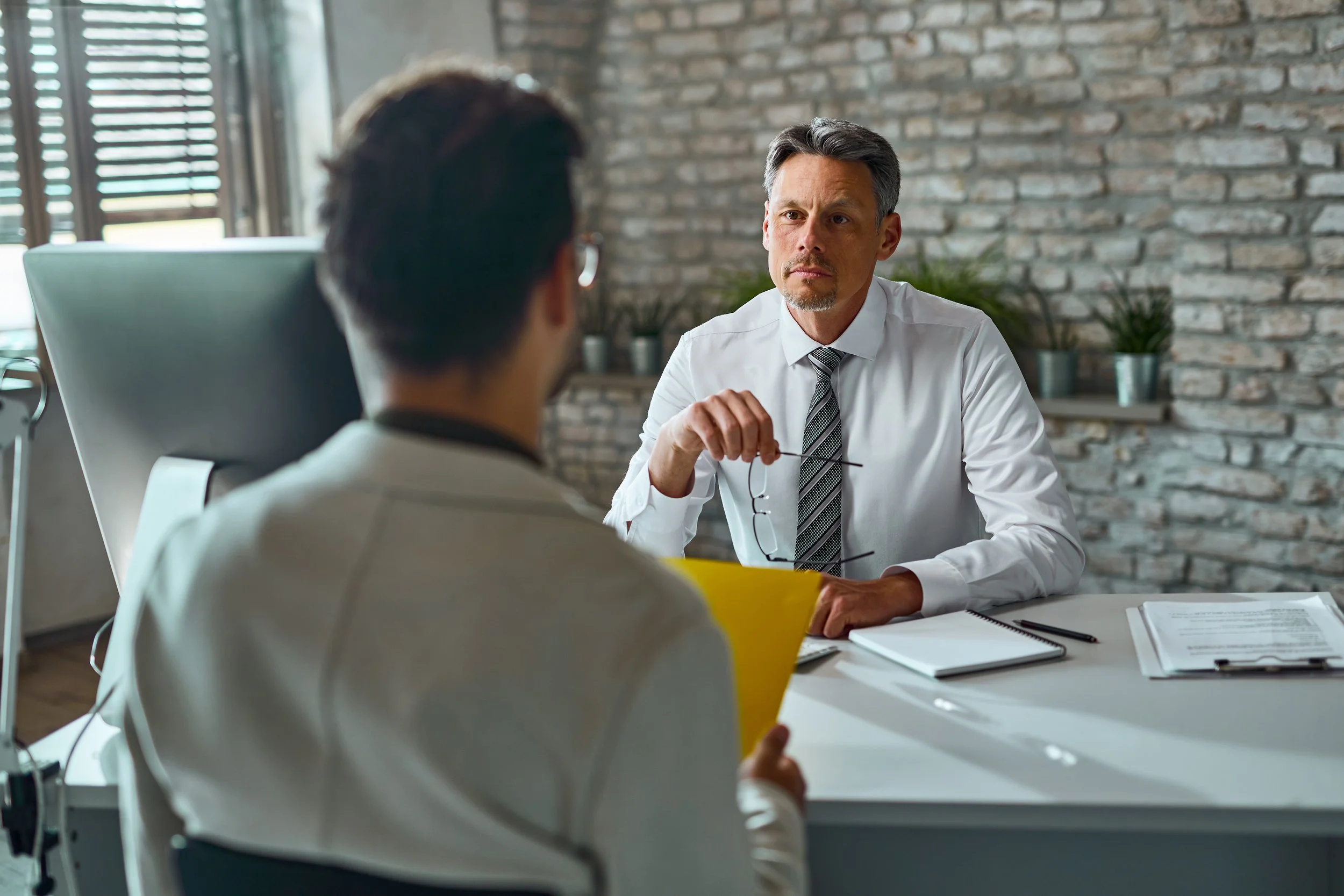 A job candidate sits across from an interviewer in an office, holding a resume while discussing qualifications during a professional interview.