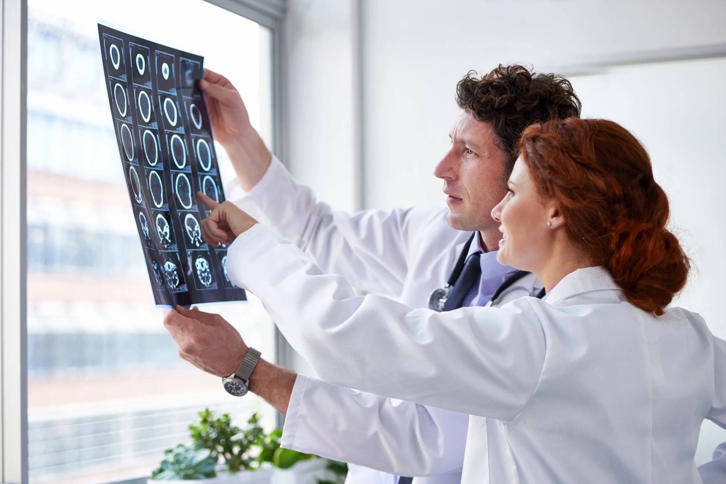 Two doctors in white coats reviewing and pointing at brain scan images together.