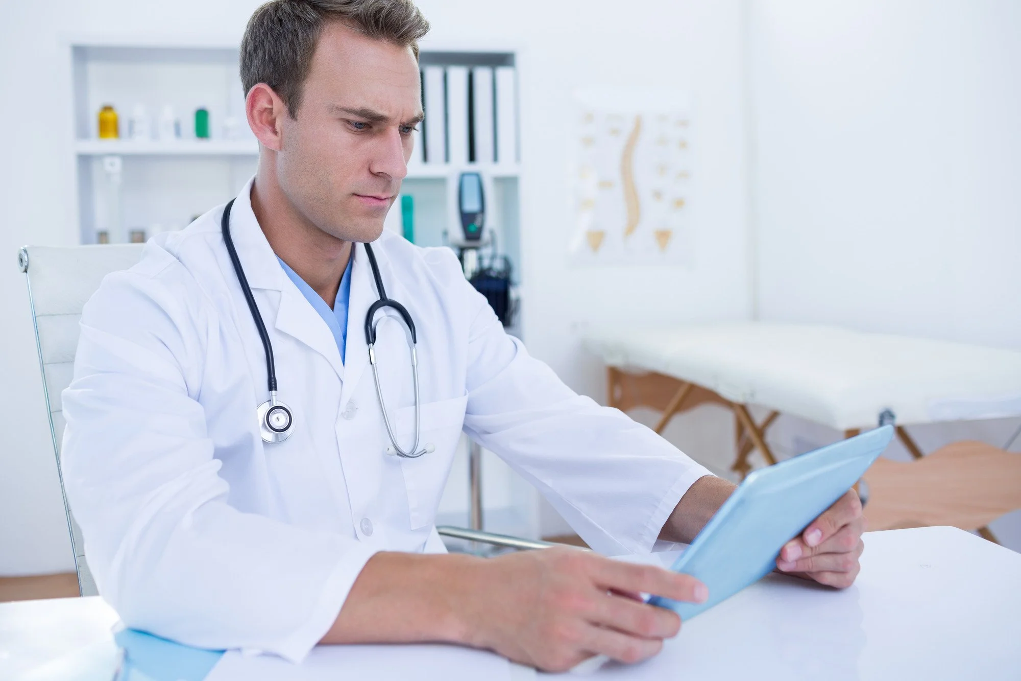 Doctor in a white coat reviewing information on a tablet in a medical office.