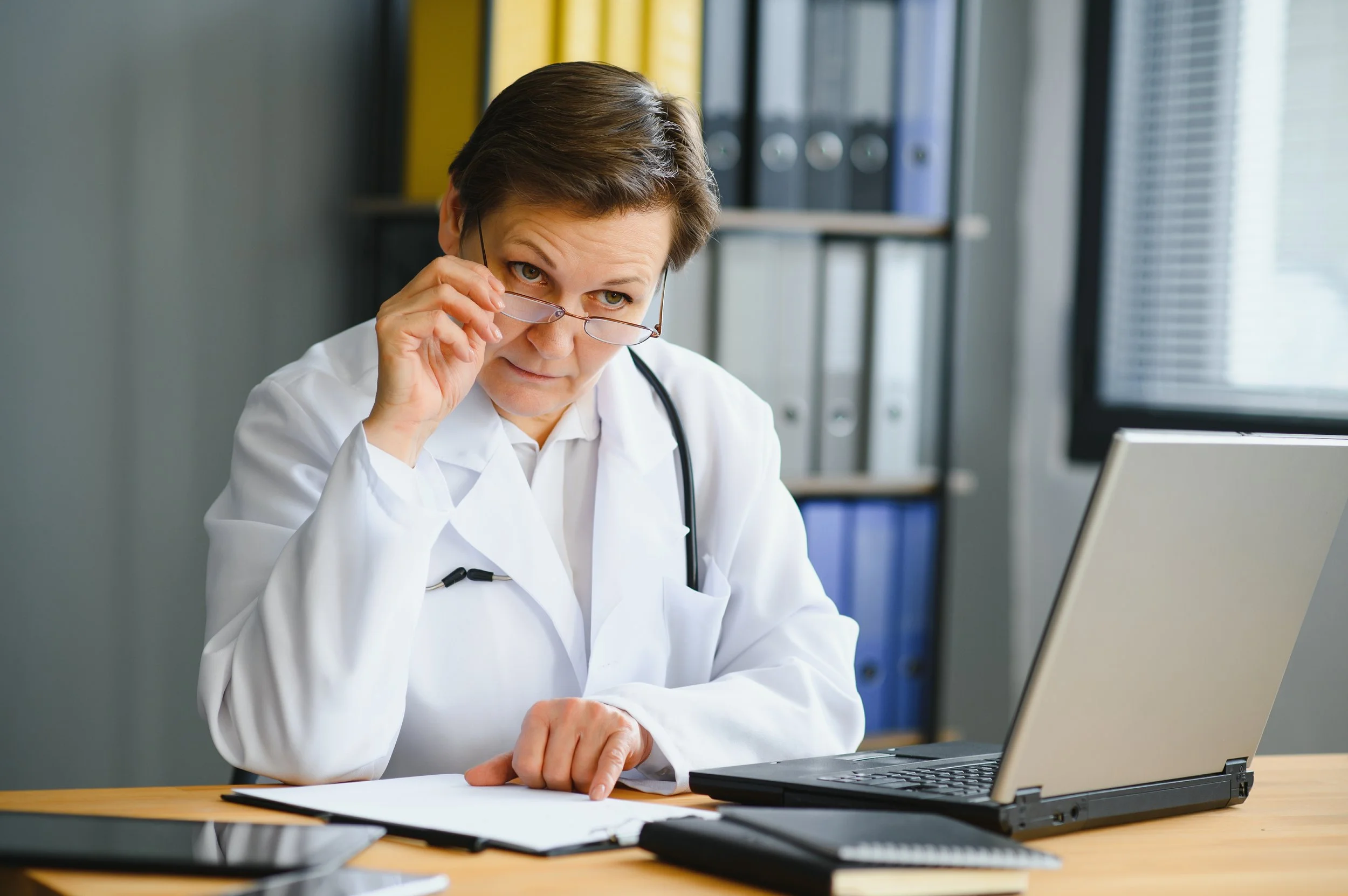 Doctor reviewing paperwork at a desk with a laptop in a medical office.